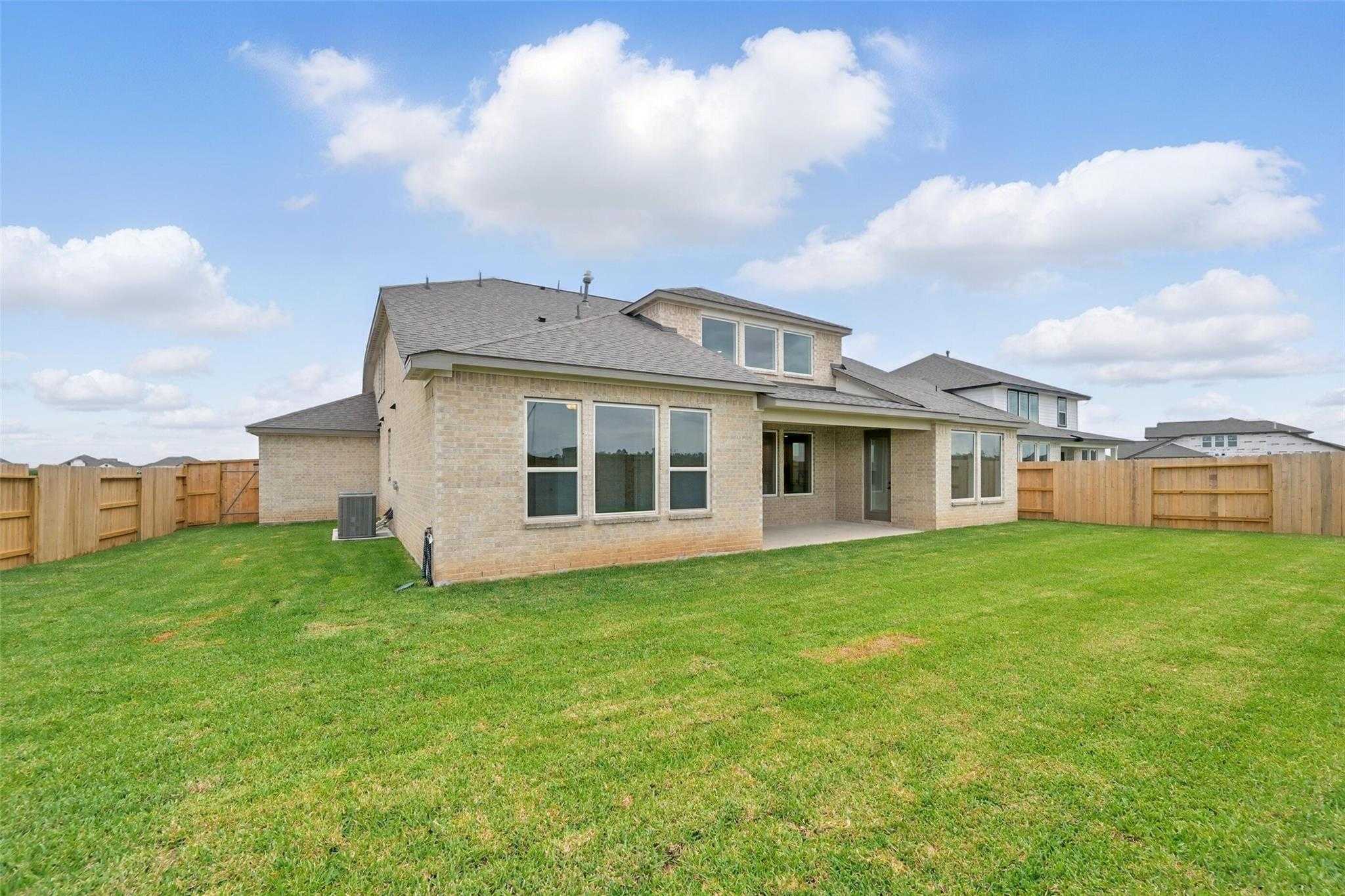 Two-story beige brick home with covered patio, lush green backyard, and privacy fence in Lago Mar, Texas City, Texas