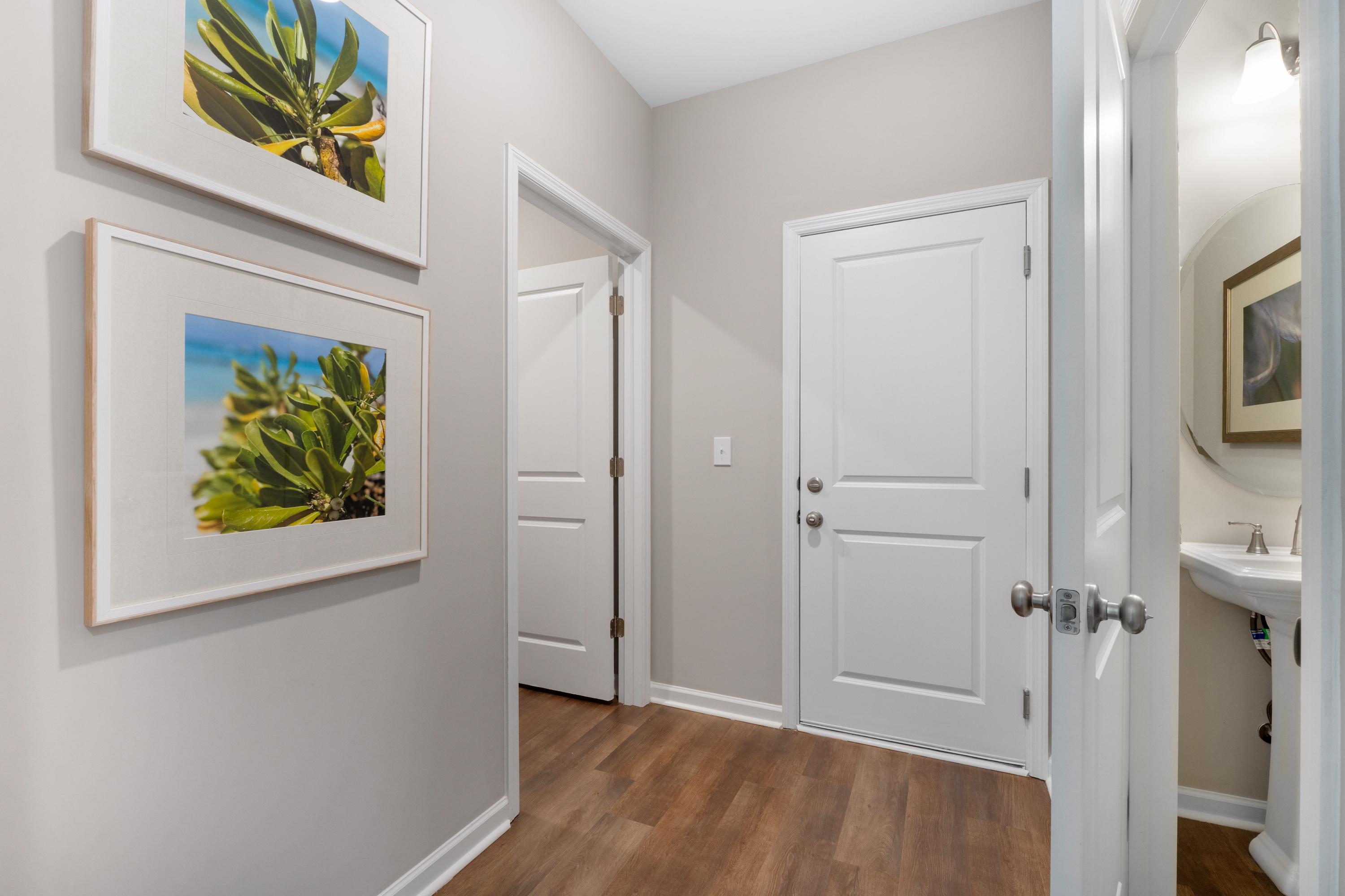 Spacious hallway interior at Evergreen Mill in Madison Alabama with tropical framed art, white doors, and powder room sink