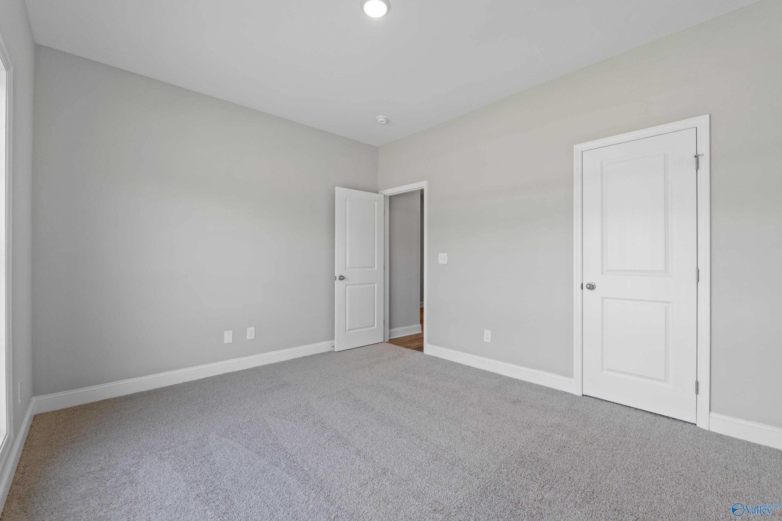 Spacious empty bedroom with light gray walls, gray carpet, and white doors in Davidson Homes The Daphne C, Athens AL