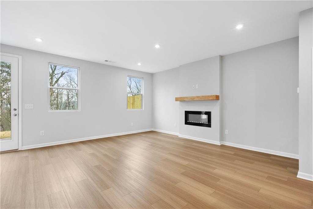 Bright living room with modern linear fireplace, hardwood floors, large windows, and sliding door in Davidson Homes Durant A, Emerson, GA