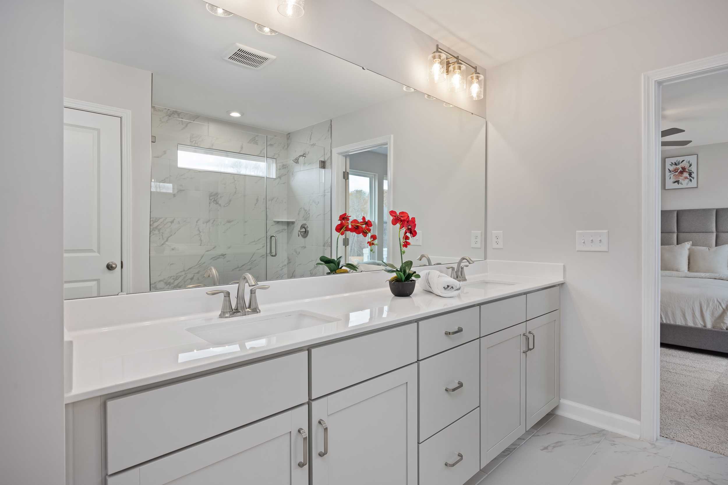 Spacious master bathroom at Enclave at Belmont in Belmont NC with double white vanity, marble shower, and red floral accents