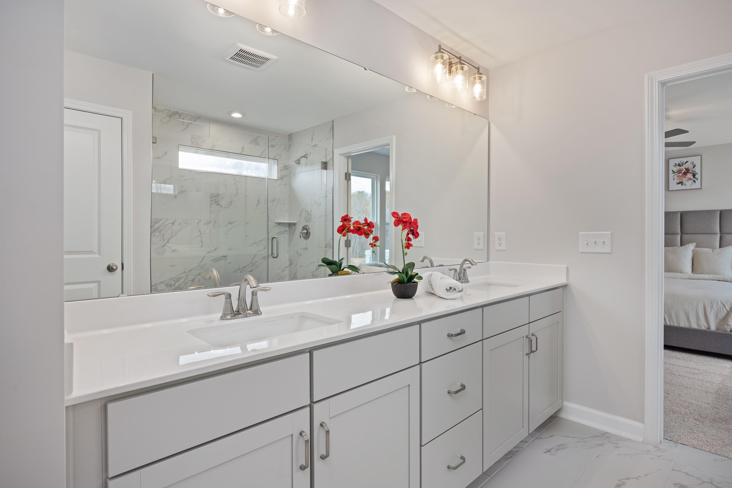 Spacious master bathroom at Enclave at Belmont in Belmont NC with double white vanity, marble shower, and red floral accents