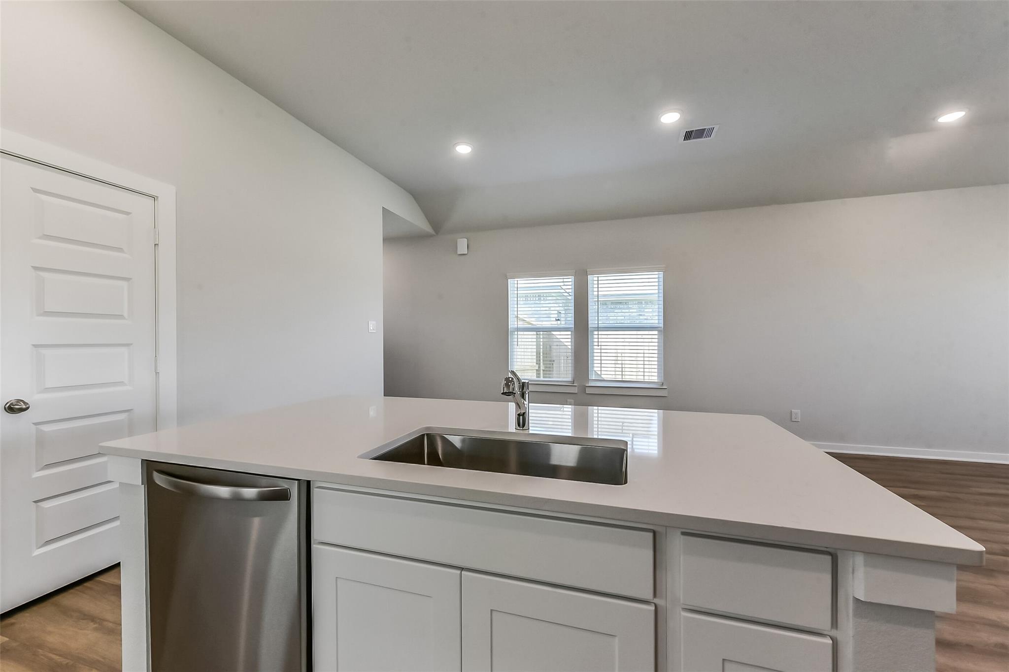 Modern kitchen island with quartz countertop, stainless steel sink, dishwasher, and white cabinets in Davidson Homes The Costa C, Dayton TX