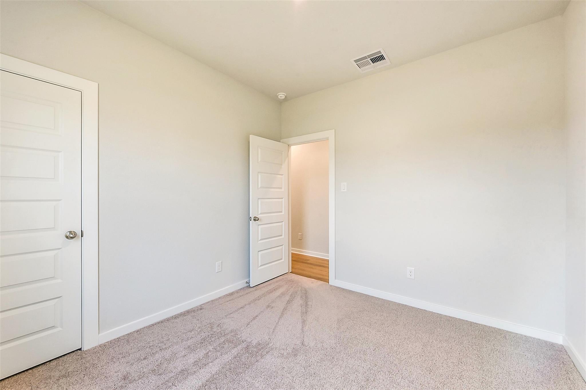 Bright secondary bedroom with beige walls, neutral carpet, and open closet door in Davidson Homes The Comal G, Dayton, Texas
