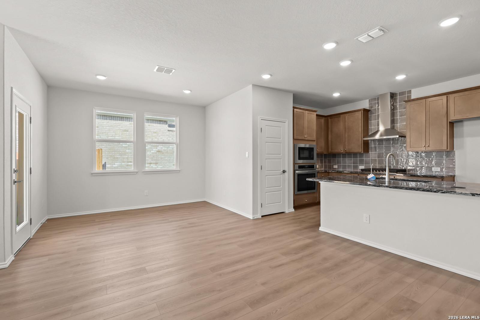 Open-concept kitchen with granite island, wood cabinets, and luxury vinyl flooring in Davidson Homes The Daphne I, San Antonio