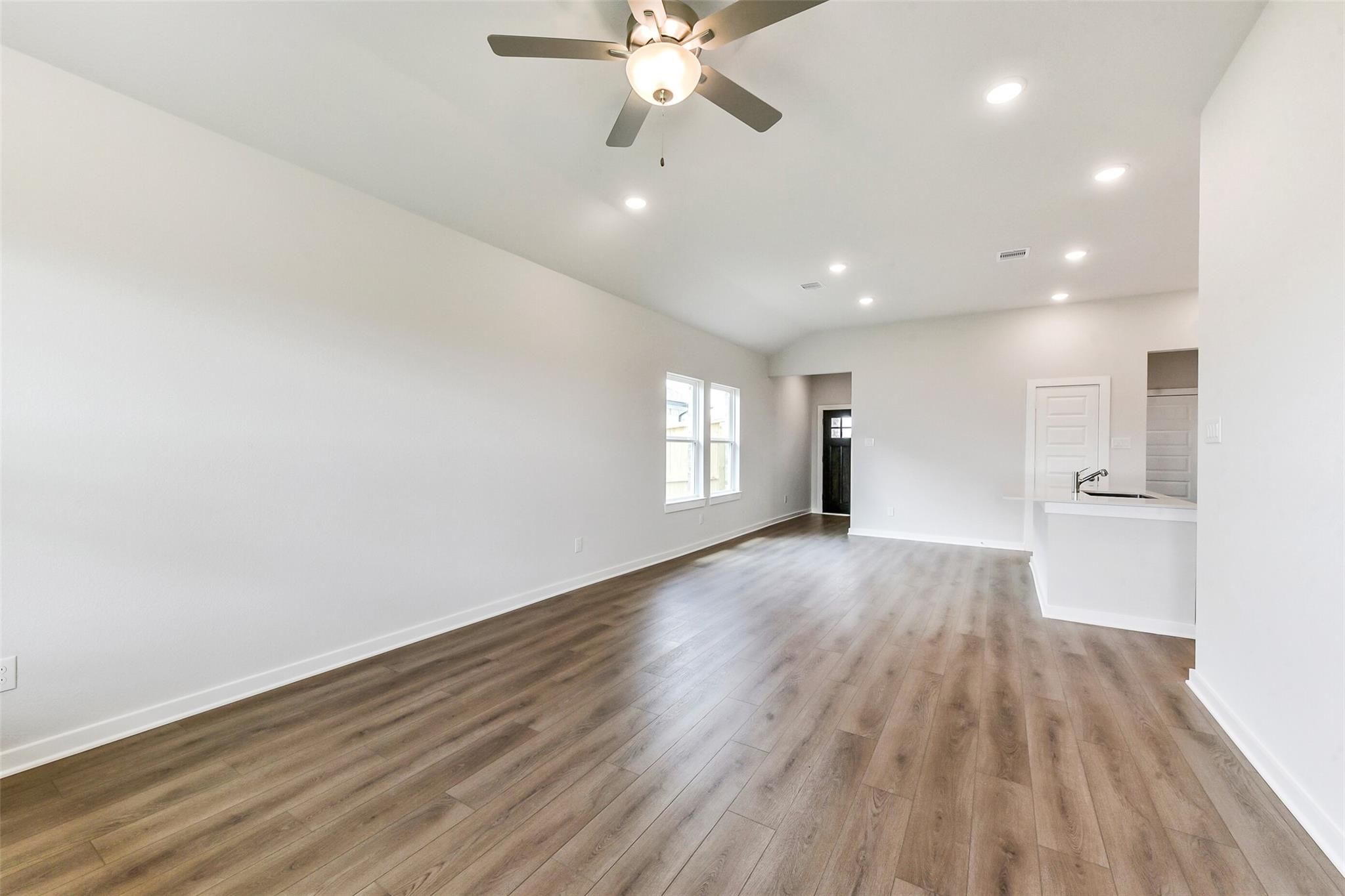 Spacious open living area with hardwood floors, ceiling fan, and adjacent kitchen in Davidson Homes Costa B 3-bedroom, Dayton Texas