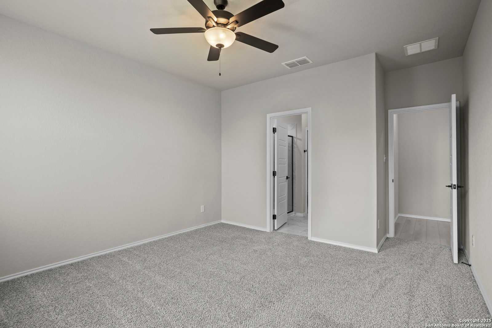 Spacious secondary bedroom with ceiling fan, gray carpet, and adjacent bath doors in Davidson Homes The Asheville E, Converse, TX