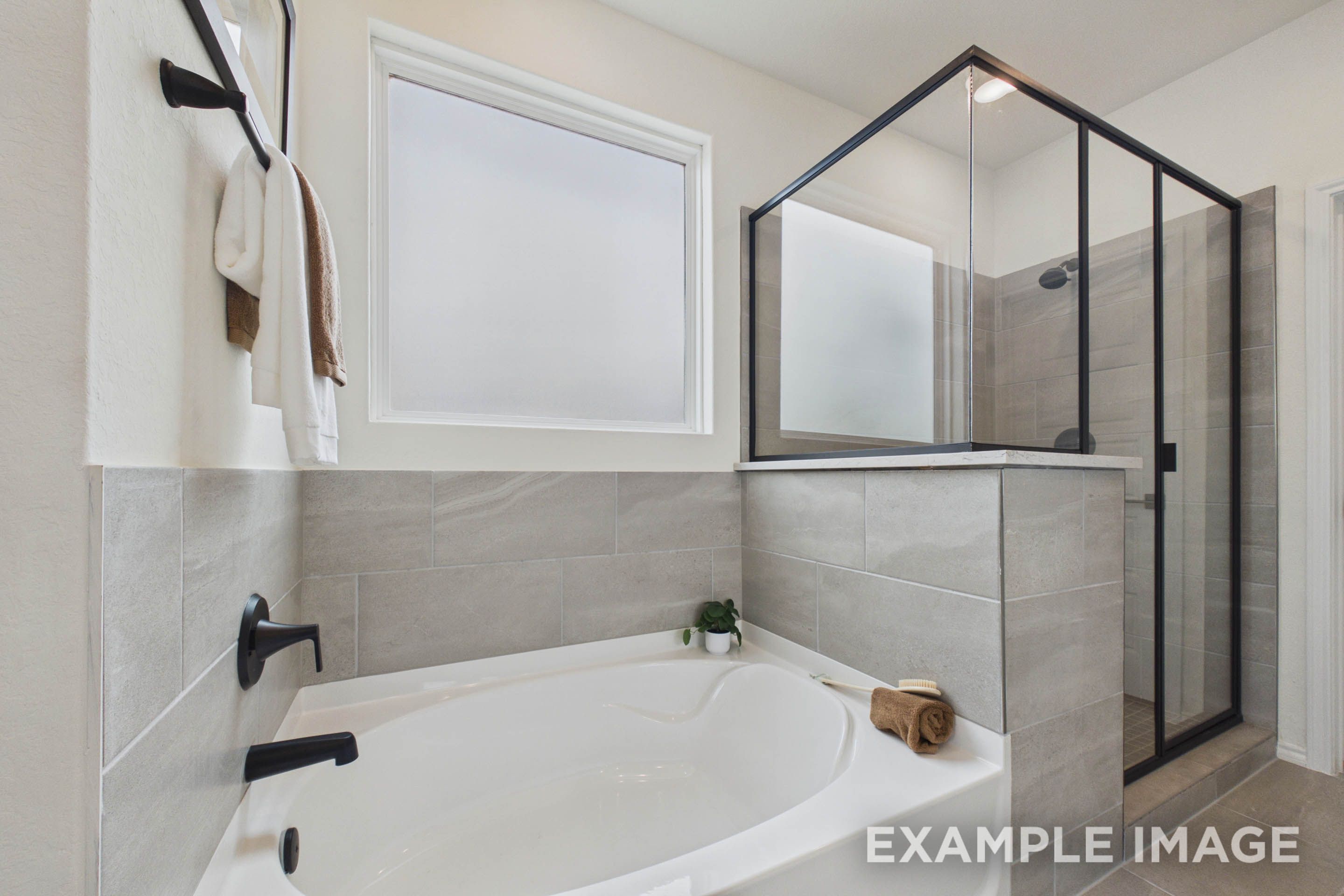 Modern master bathroom in The Laurel G featuring a soaking tub, separate glass-enclosed shower, and sleek tile finishes.