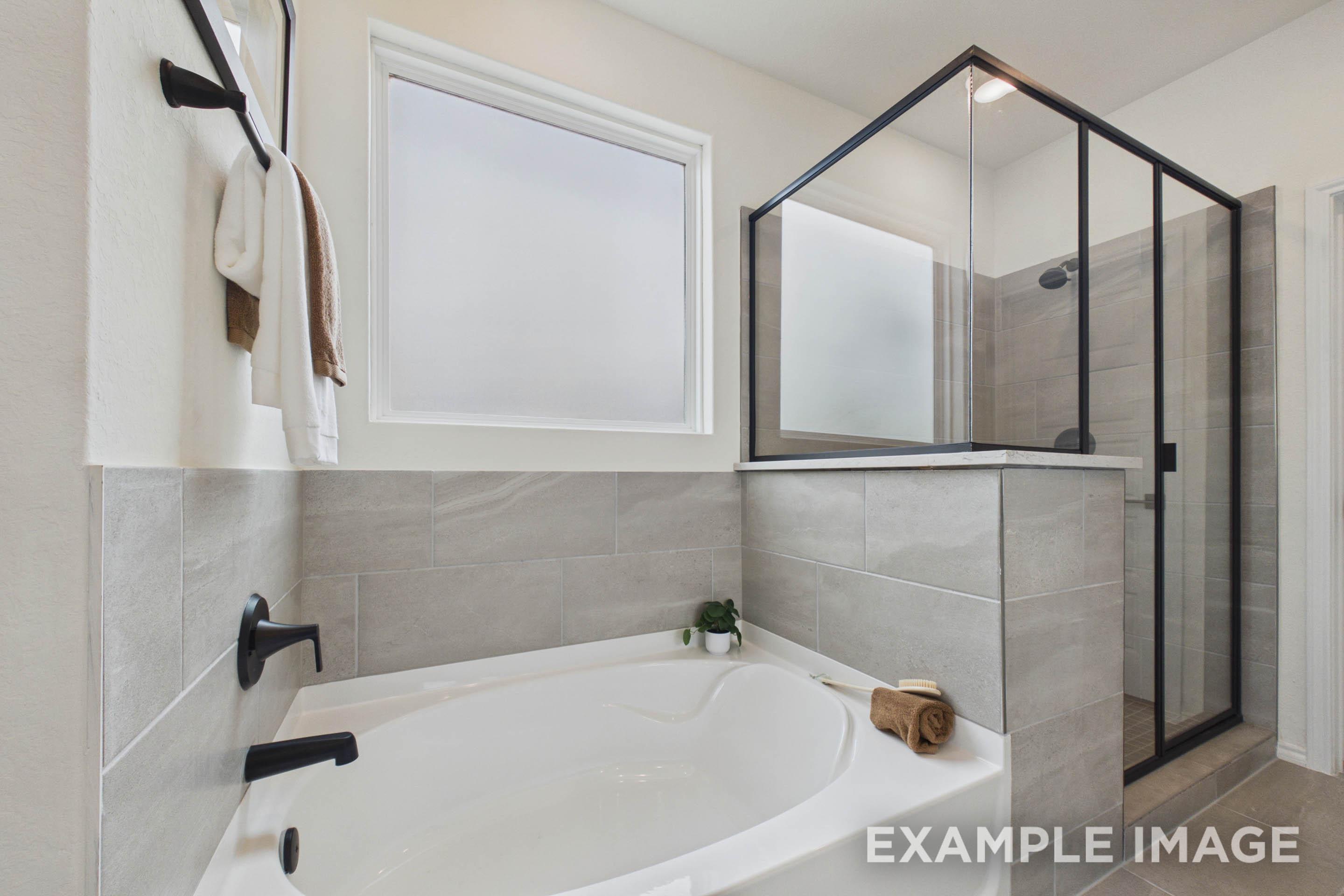 Modern master bathroom in The Laurel G featuring a soaking tub, separate glass-enclosed shower, and sleek tile finishes.