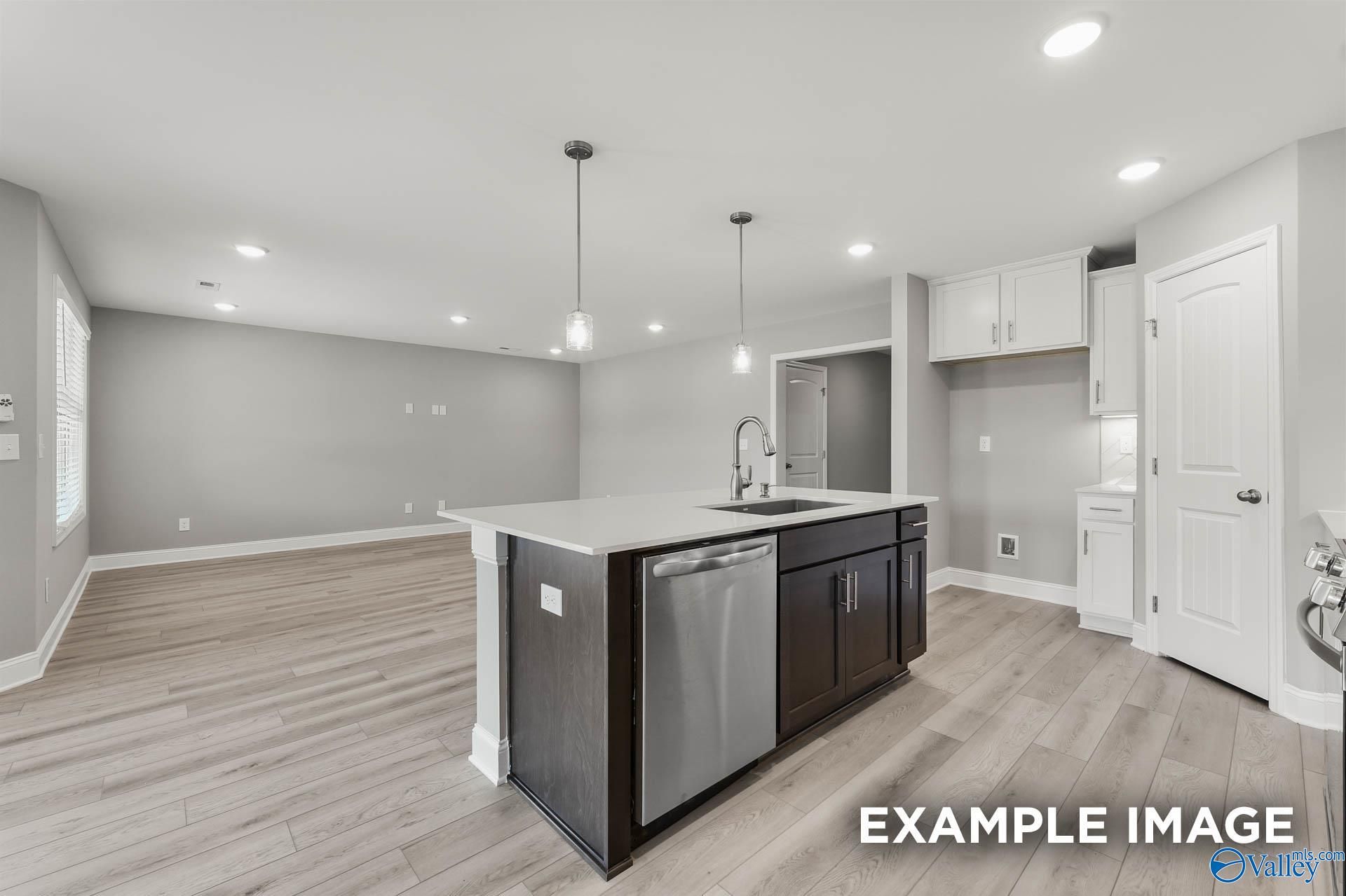 Modern open kitchen with white quartz island, stainless dishwasher, dark cabinets, hardwood floors in Everett B home, Toney, AL