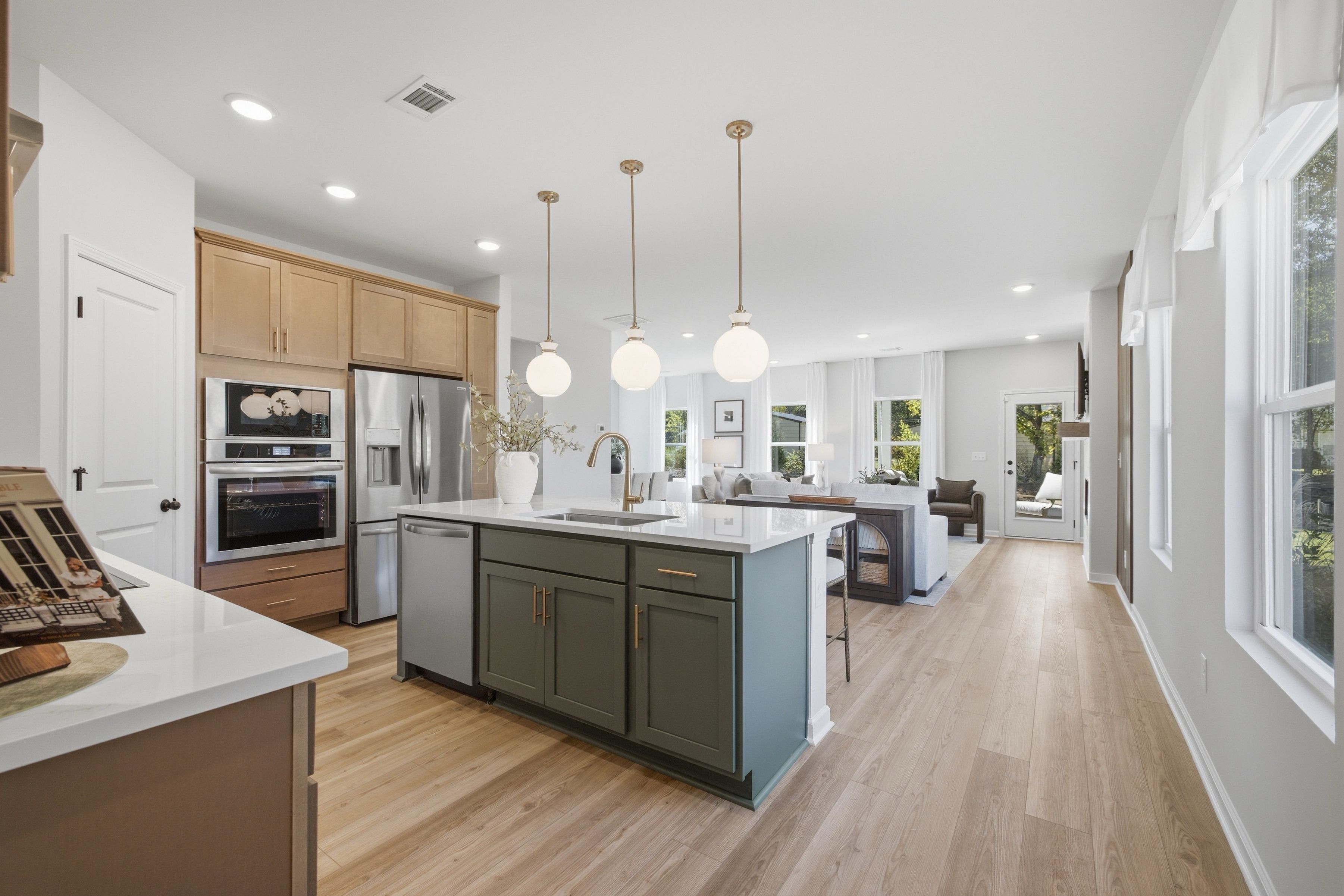 Open-concept kitchen with green island, wood cabinets, and pendant lights at Greene Farm by Davidson Homes in Cartersville, GA