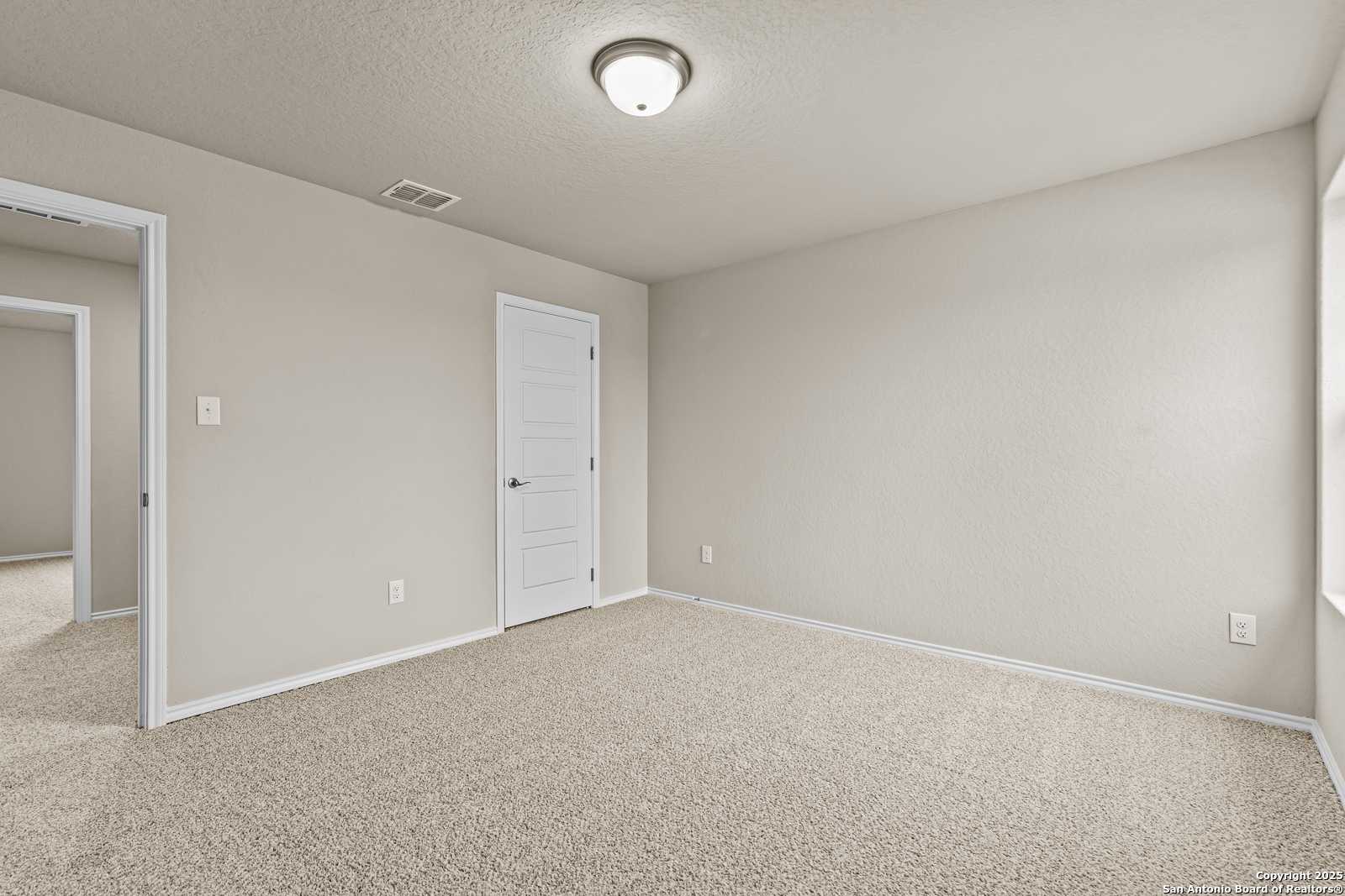 Spacious empty bedroom with beige walls, neutral carpet, and double doors in Davidson Homes The Douglas F, San Antonio