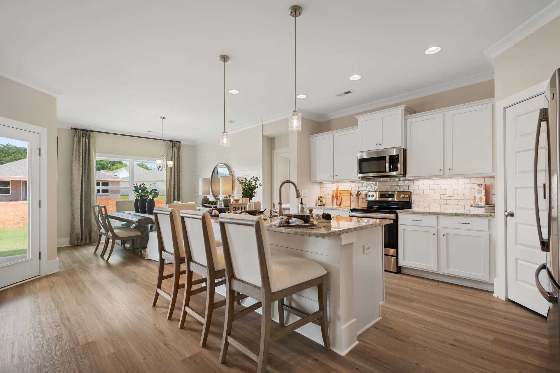Open-concept kitchen and dining area at Flint Meadows in New Market, Alabama with white cabinetry, island bar, hardwood floors