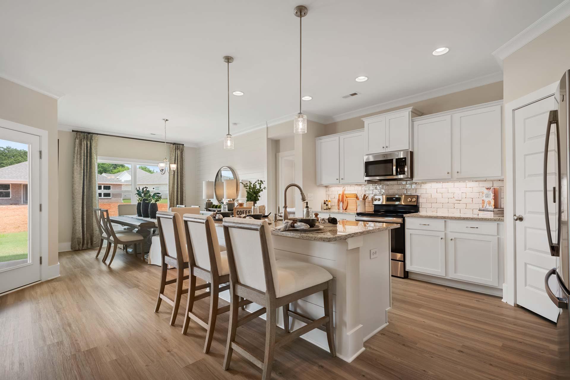 Open-concept kitchen and dining area at Flint Meadows in New Market, Alabama with white cabinetry, island bar, hardwood floors