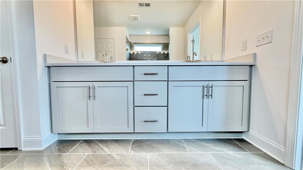 Modern double vanity with gray cabinets and stone tile flooring in The Hickory C floor plan, Wehunt Meadows, Hoschton, GA.