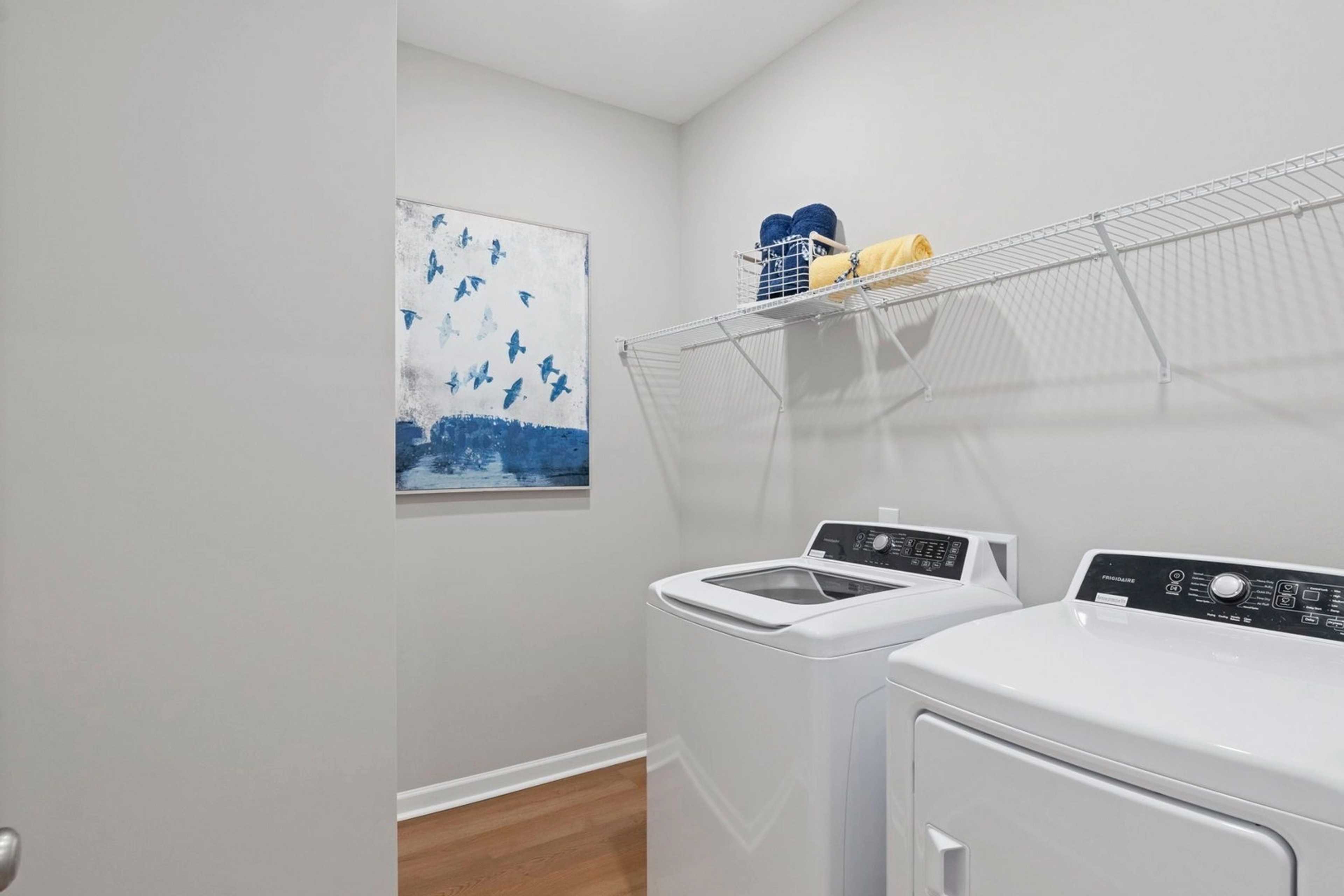 Laundry room at Bailey Park in Fayetteville Tennessee with white washer dryer, wire shelving, blue towels, and abstract art