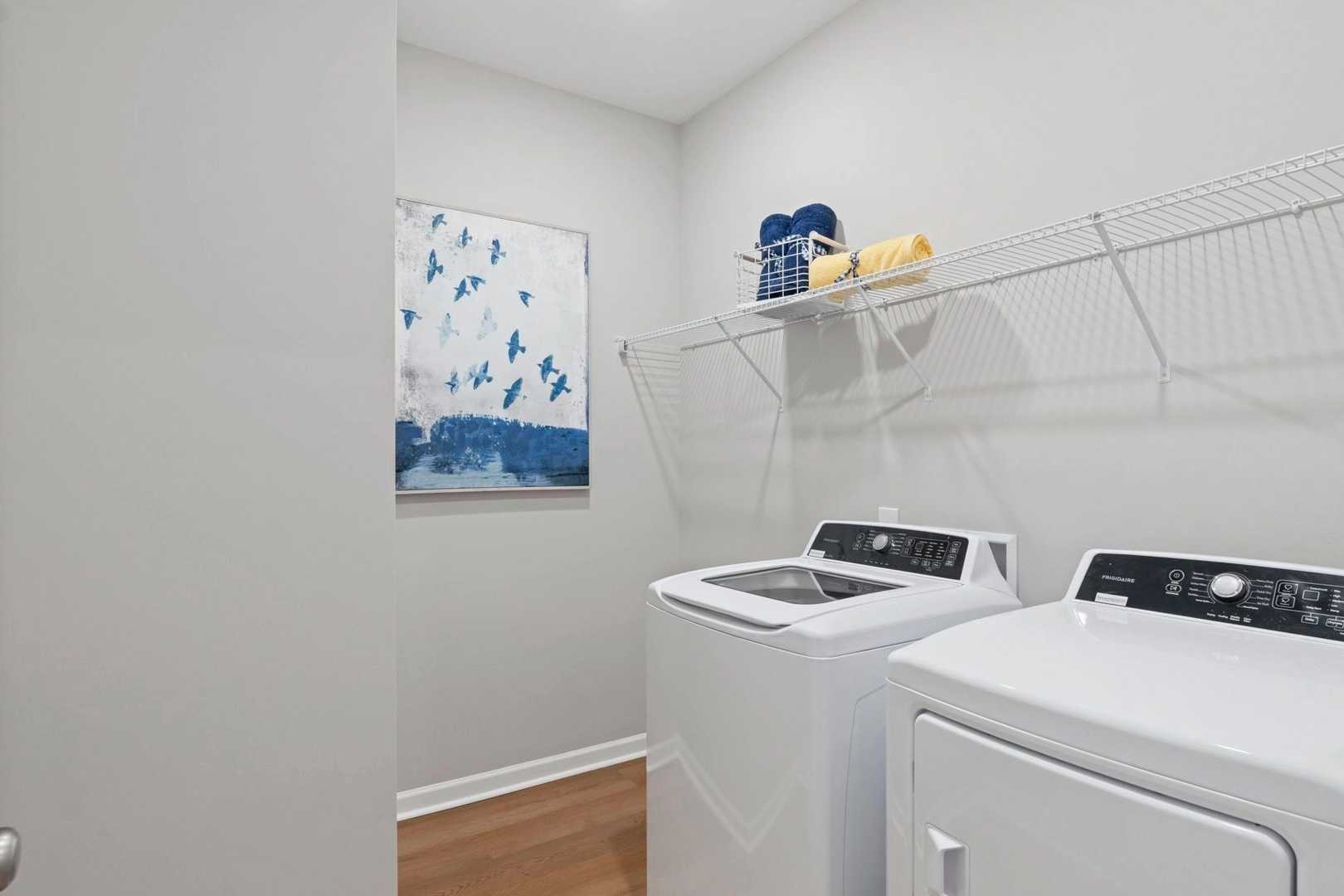 Laundry room at Bailey Park in Fayetteville Tennessee with white washer dryer, wire shelving, blue towels, and abstract art