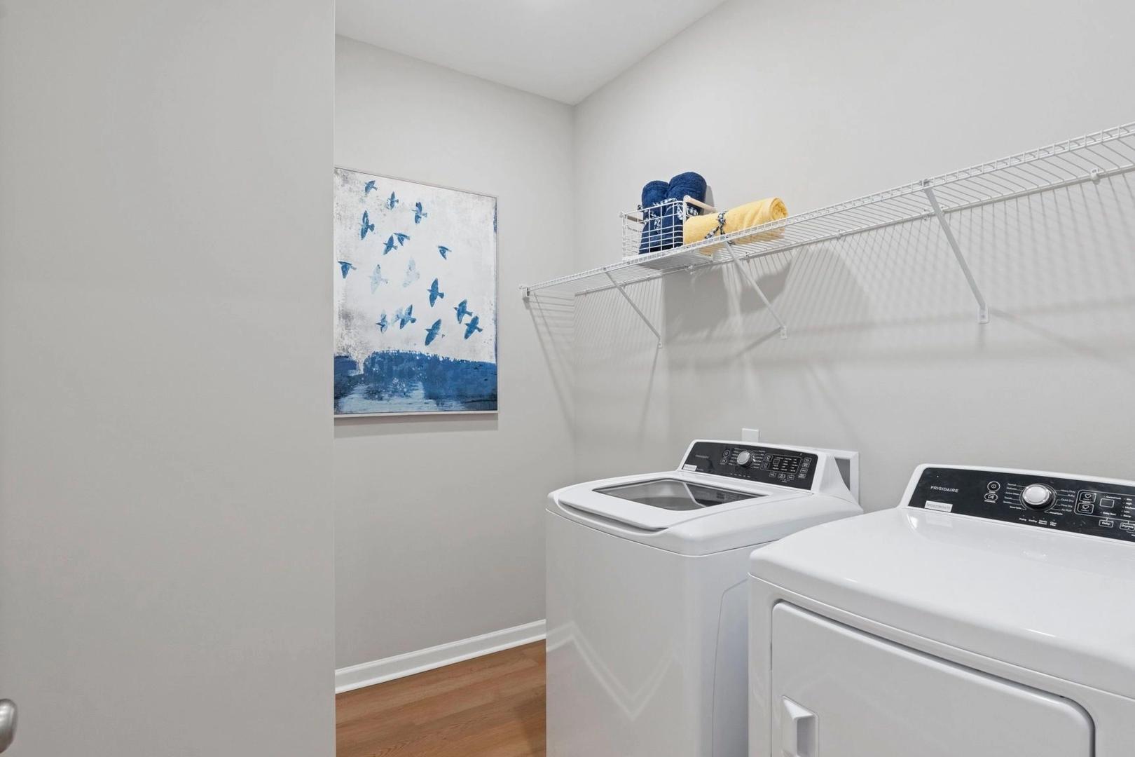 Laundry room at Bailey Park in Fayetteville Tennessee with white washer dryer, wire shelving, blue towels, and abstract art