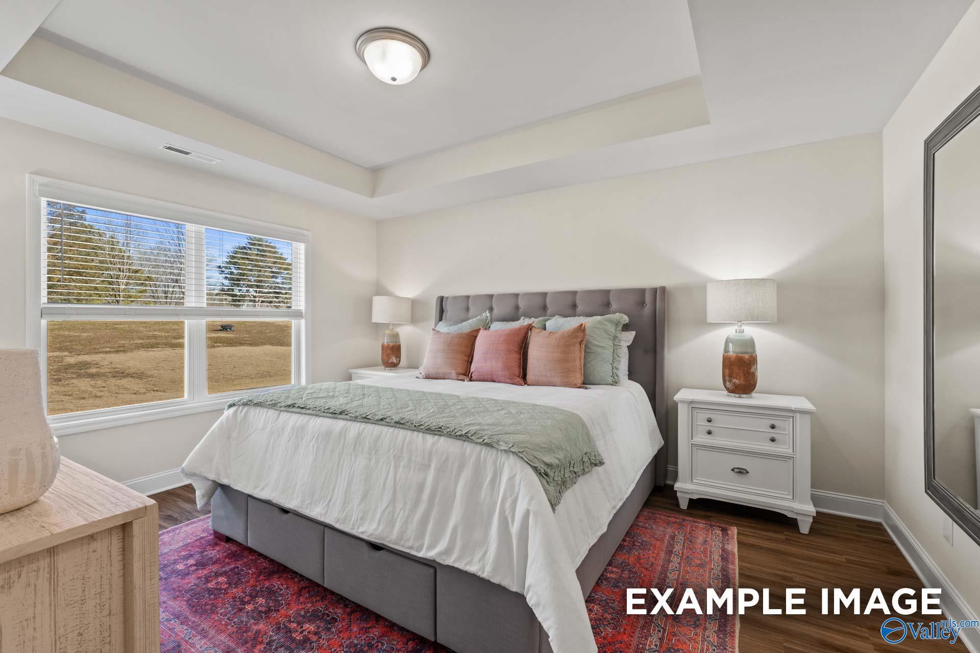 Elegant master bedroom with gray tufted bed, tray ceiling, and window view in Davidson Homes The Franklin C, New Market, Alabama