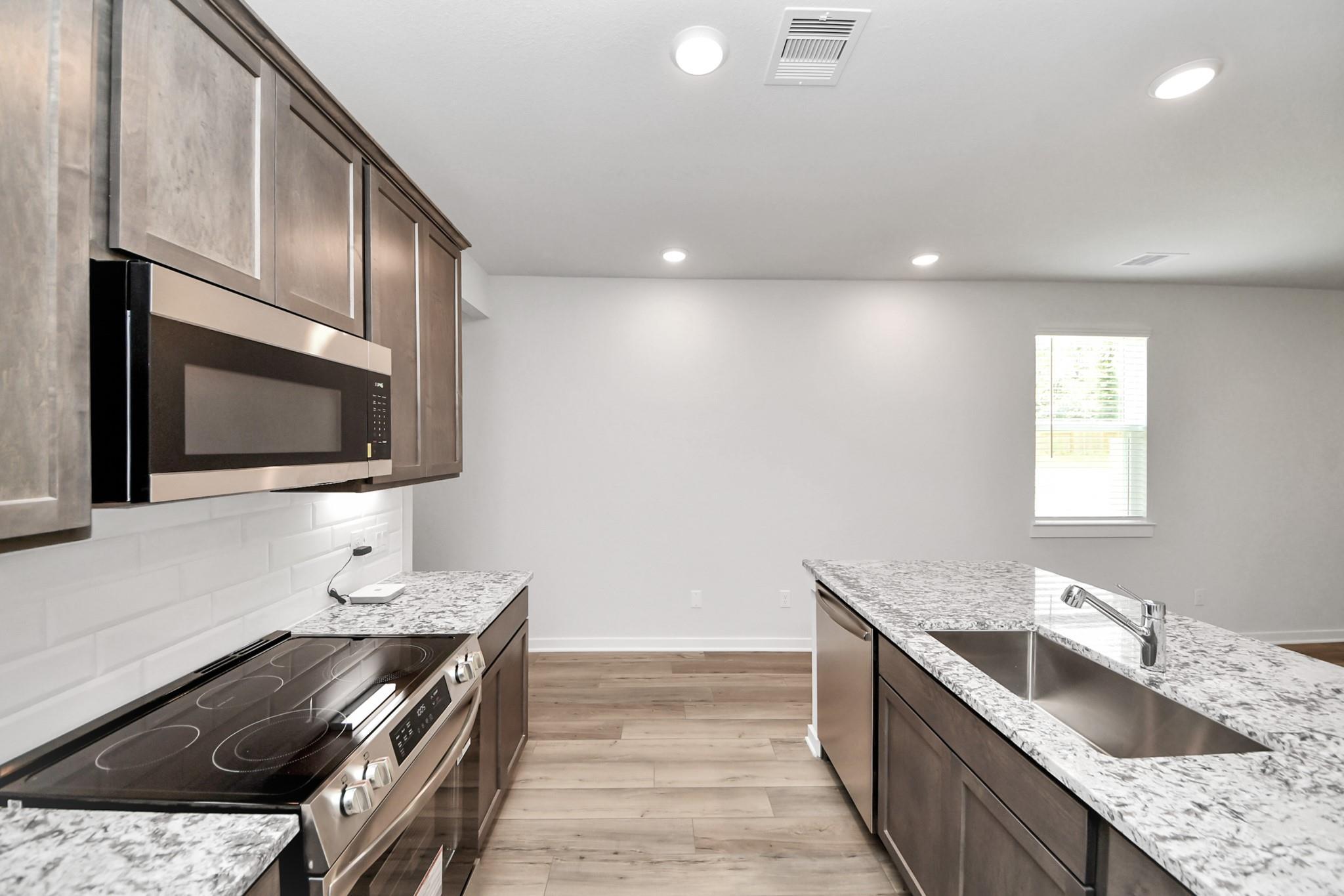 Modern kitchen with granite countertops, stainless appliances, and island in The Sabine E floor plan, Liberty Estates.