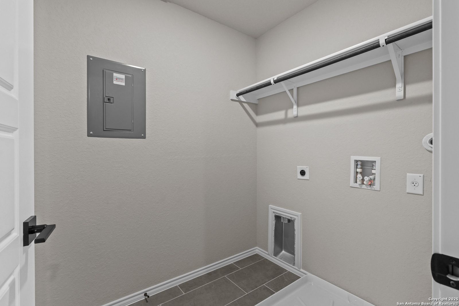 Functional laundry room featuring white open shelves, washer-dryer hookups, electrical panel, and pet door in Davidson Homes The Charlotte B, San Antonio
