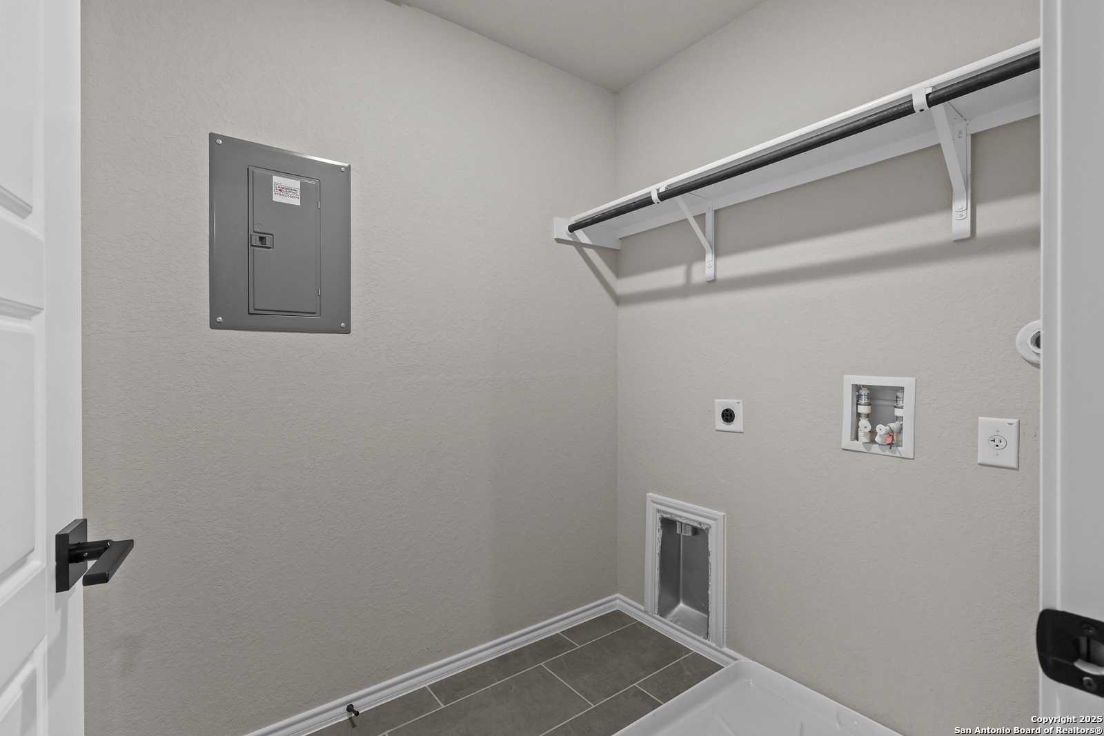 Functional laundry room featuring white open shelves, washer-dryer hookups, electrical panel, and pet door in Davidson Homes The Charlotte B, San Antonio