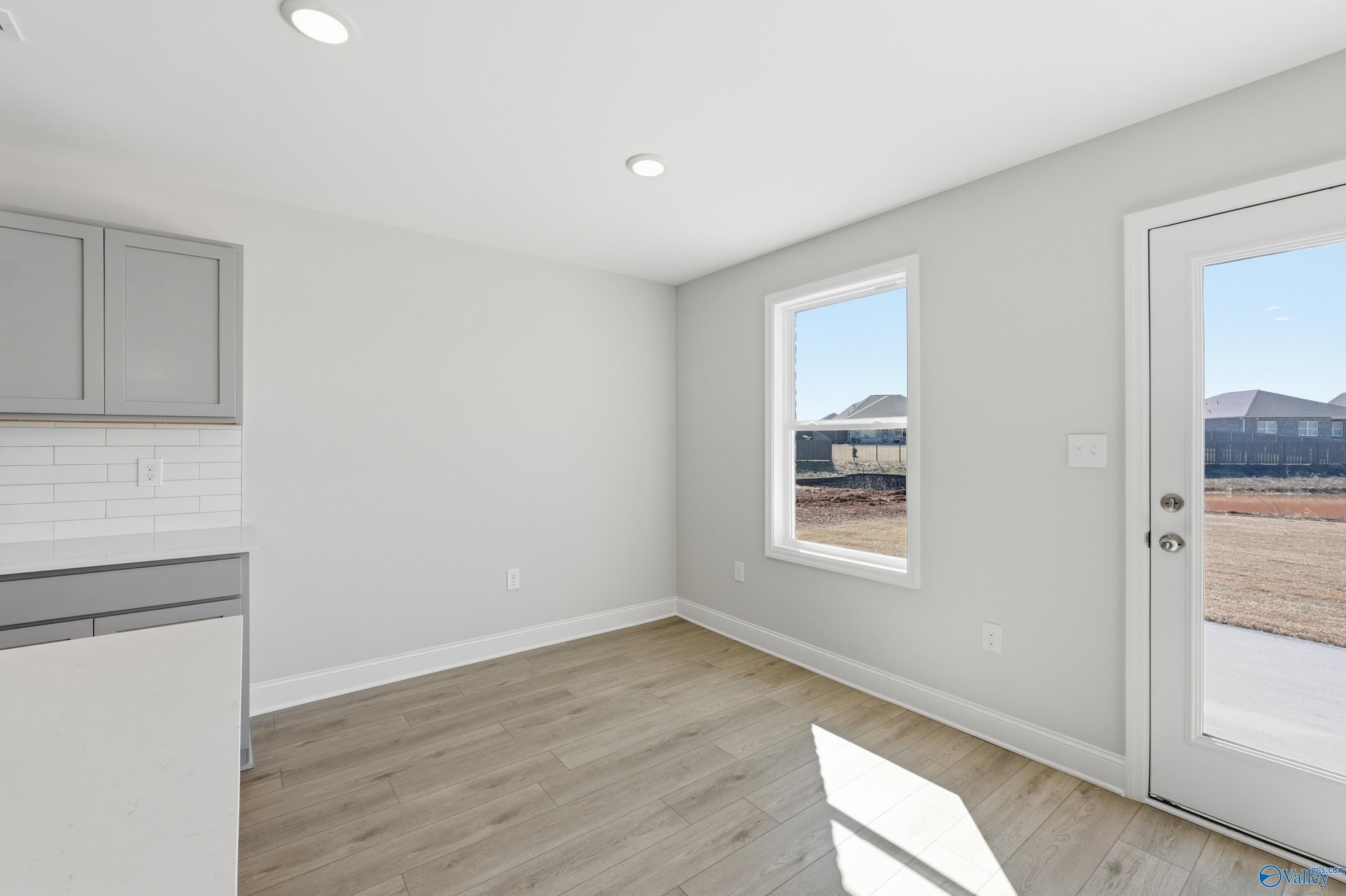 Bright laundry room with gray shaker cabinets, utility sink, dishwasher, and sliding glass door to backyard in Davidson Homes The Butler, New Market, Alabama