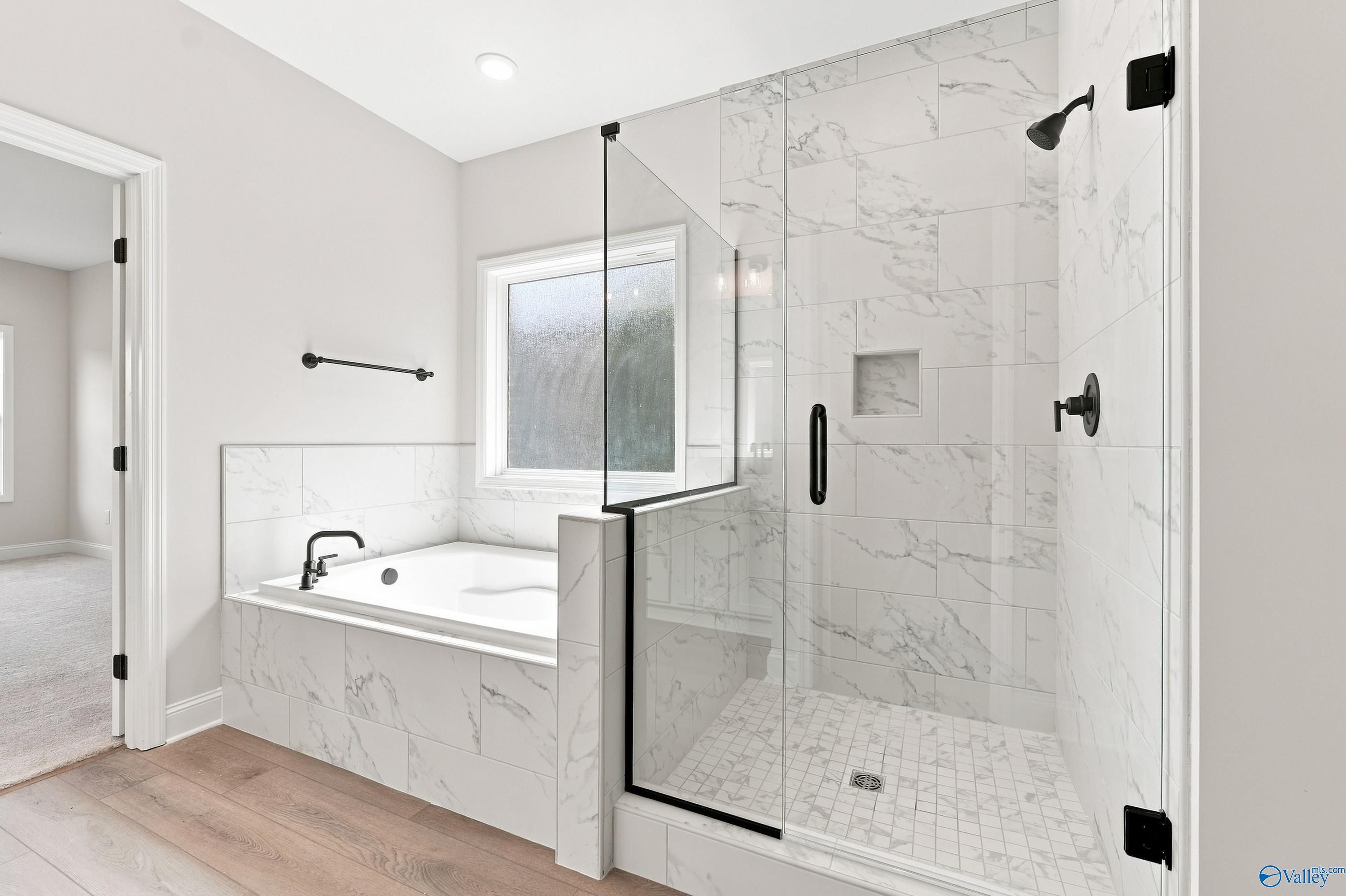 Modern primary bathroom with marble-tiled soaking tub and glass-enclosed shower in Rockford B plan, Kendall Downs, Toney, AL.