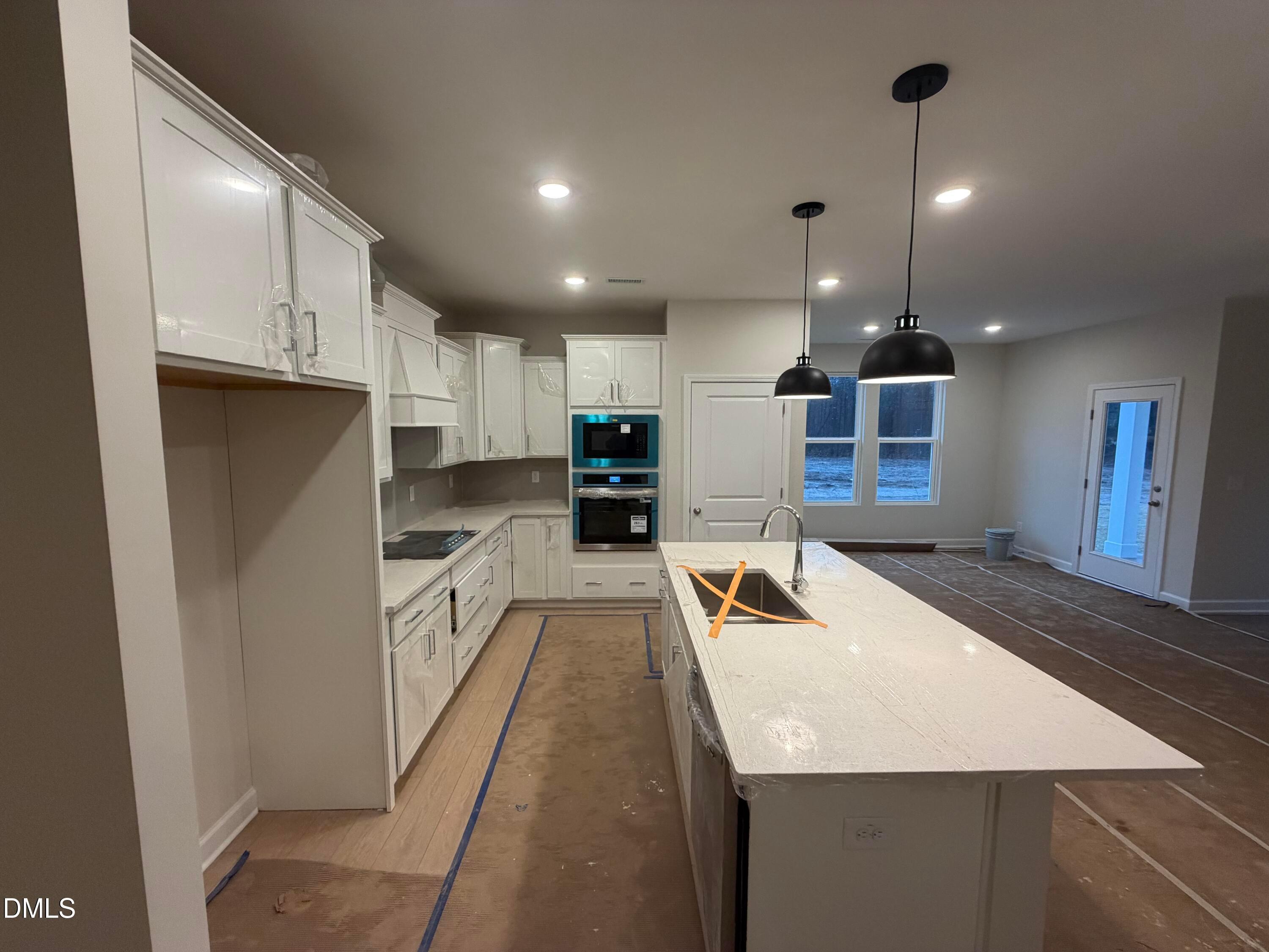 Modern white kitchen with quartz island, blue double oven, stainless appliances, and pendant lights in The Daphne C by Davidson Homes, Lillington, NC