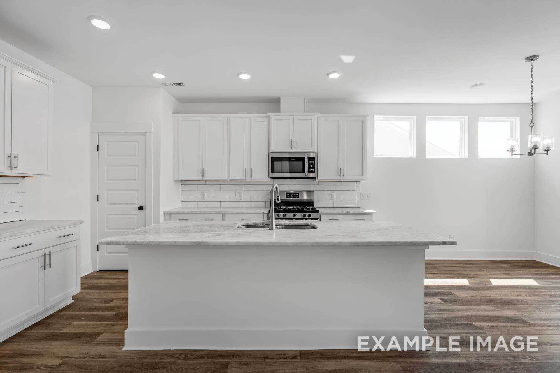 Modern white kitchen in The Ash C featuring large island with marble top, stainless appliances, and hardwood floors