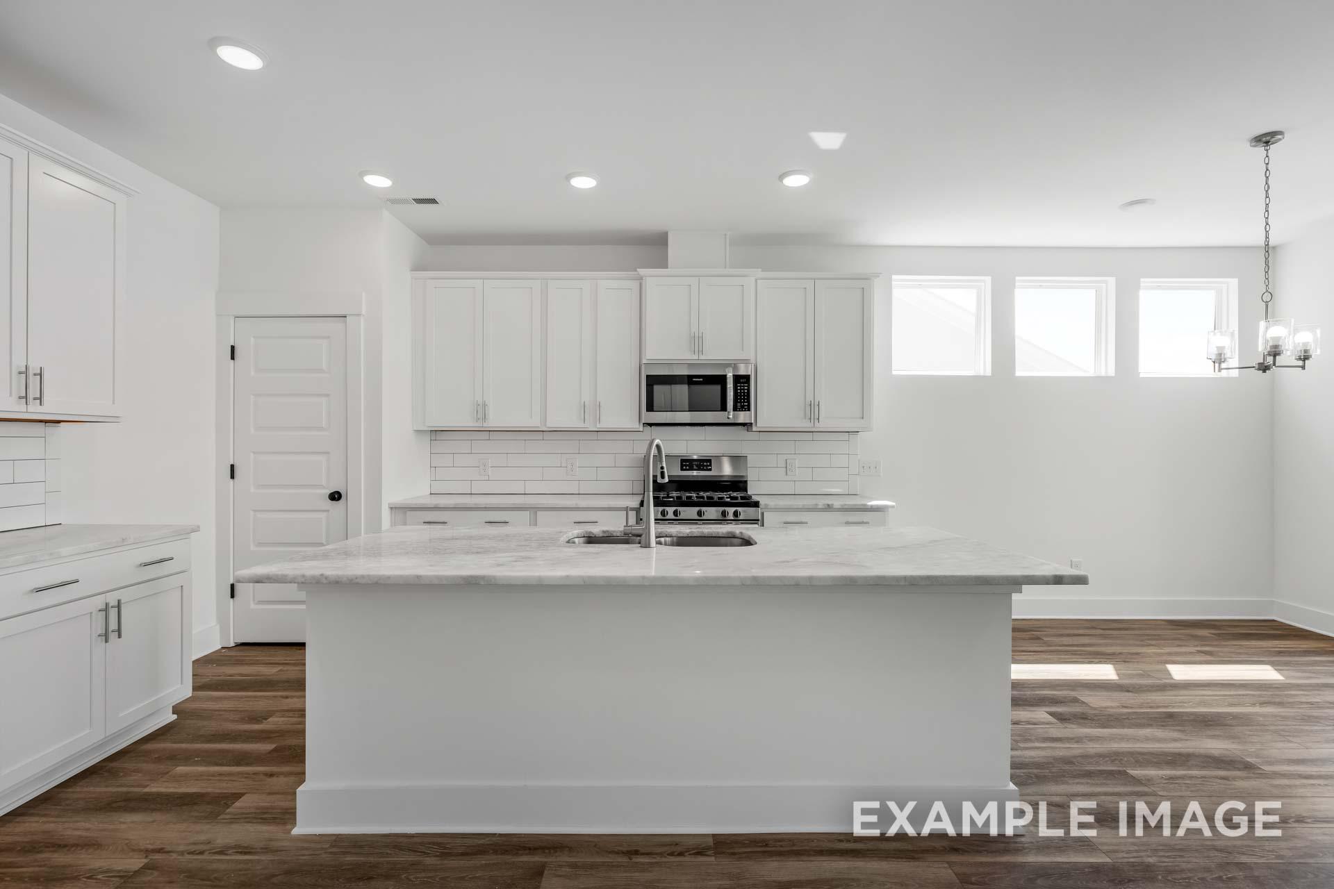 Modern white kitchen in The Ash C featuring large island with marble top, stainless appliances, and hardwood floors