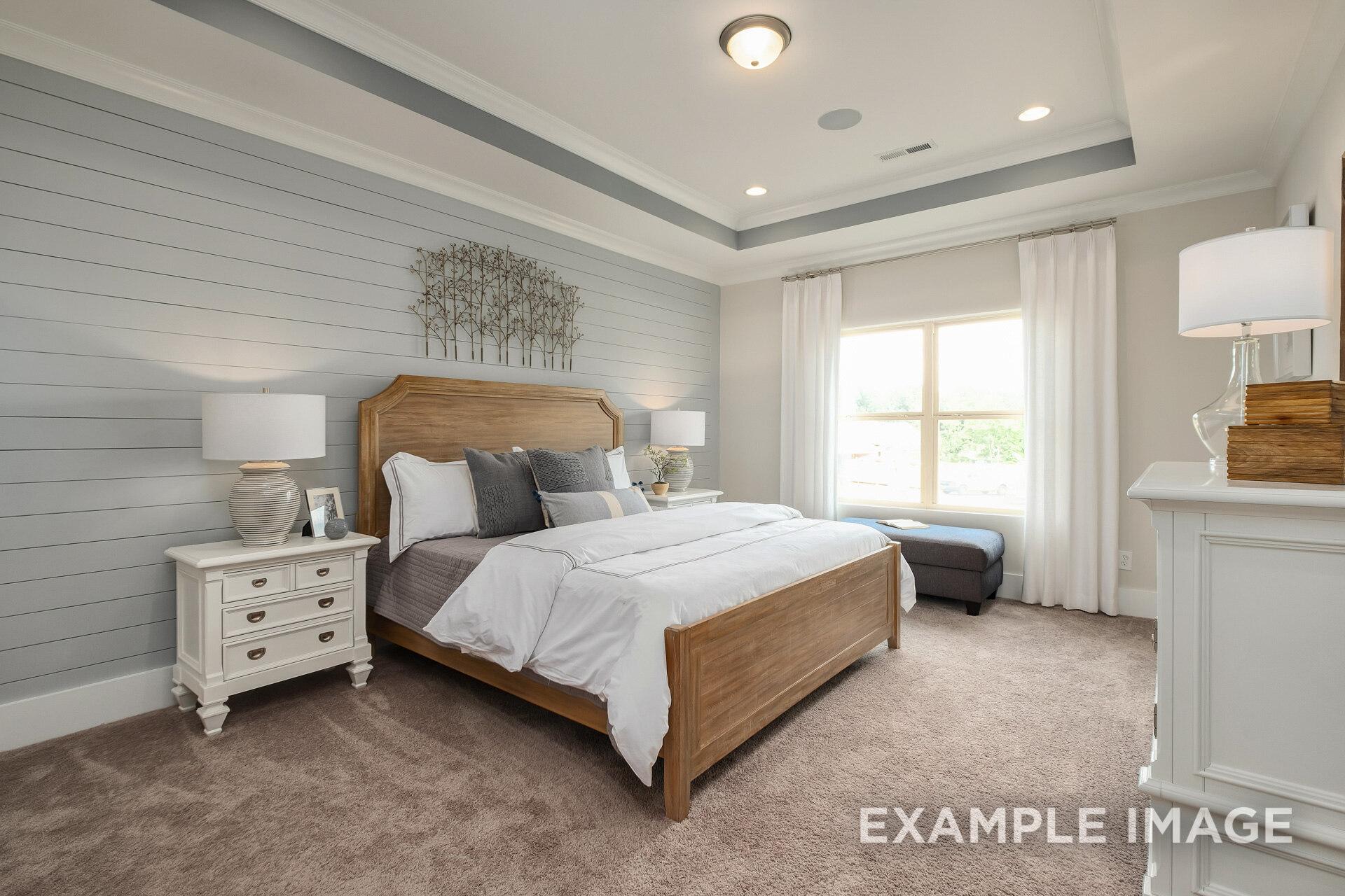 Master bedroom in The Daphne D with wooden bed frame, neutral gray walls, bedside lamps, and large window seat