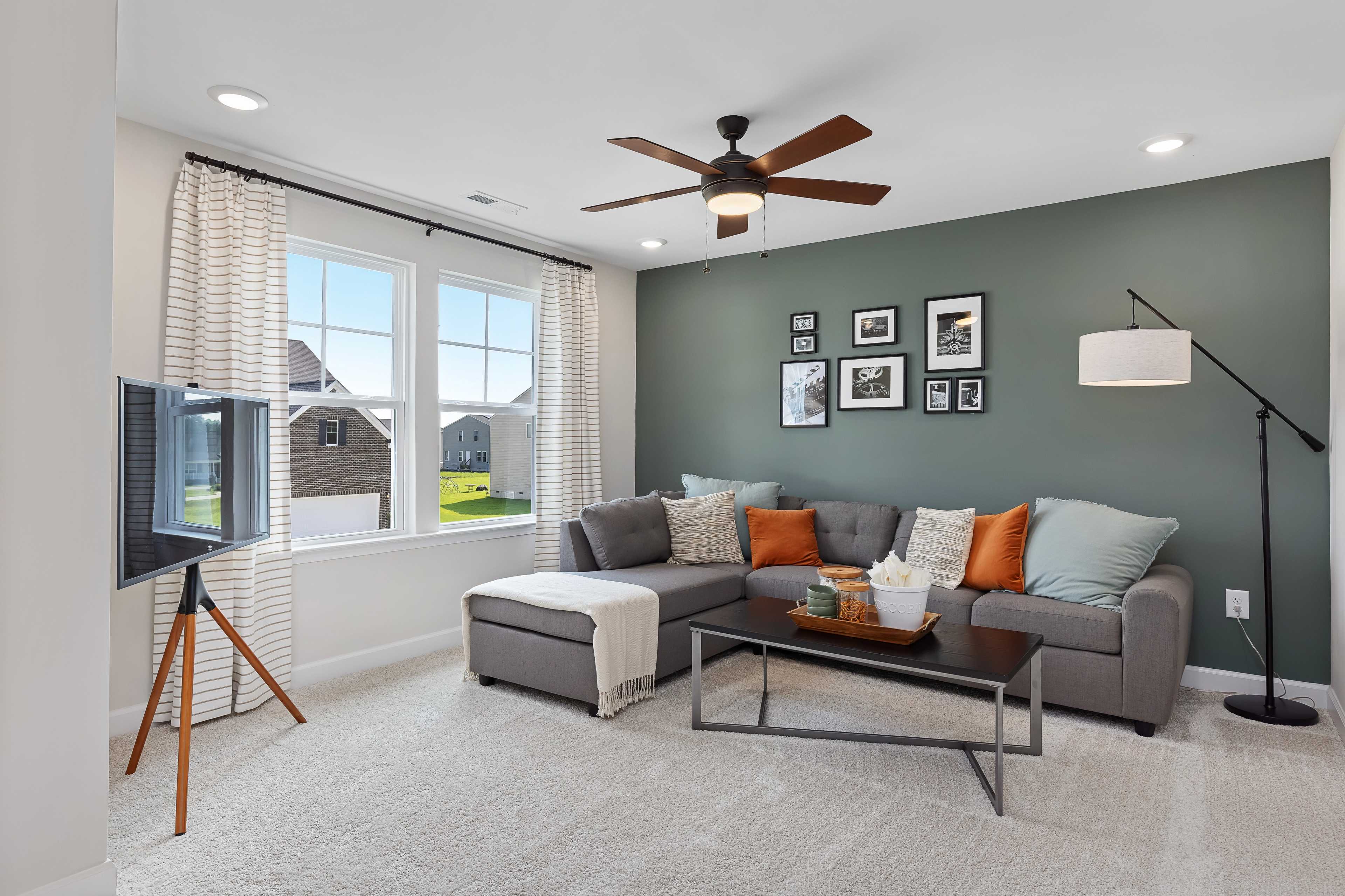 Cozy living room with gray L-shaped sofa, orange pillows, wall art, and large windows at Woodland Crossing in Zebulon, NC