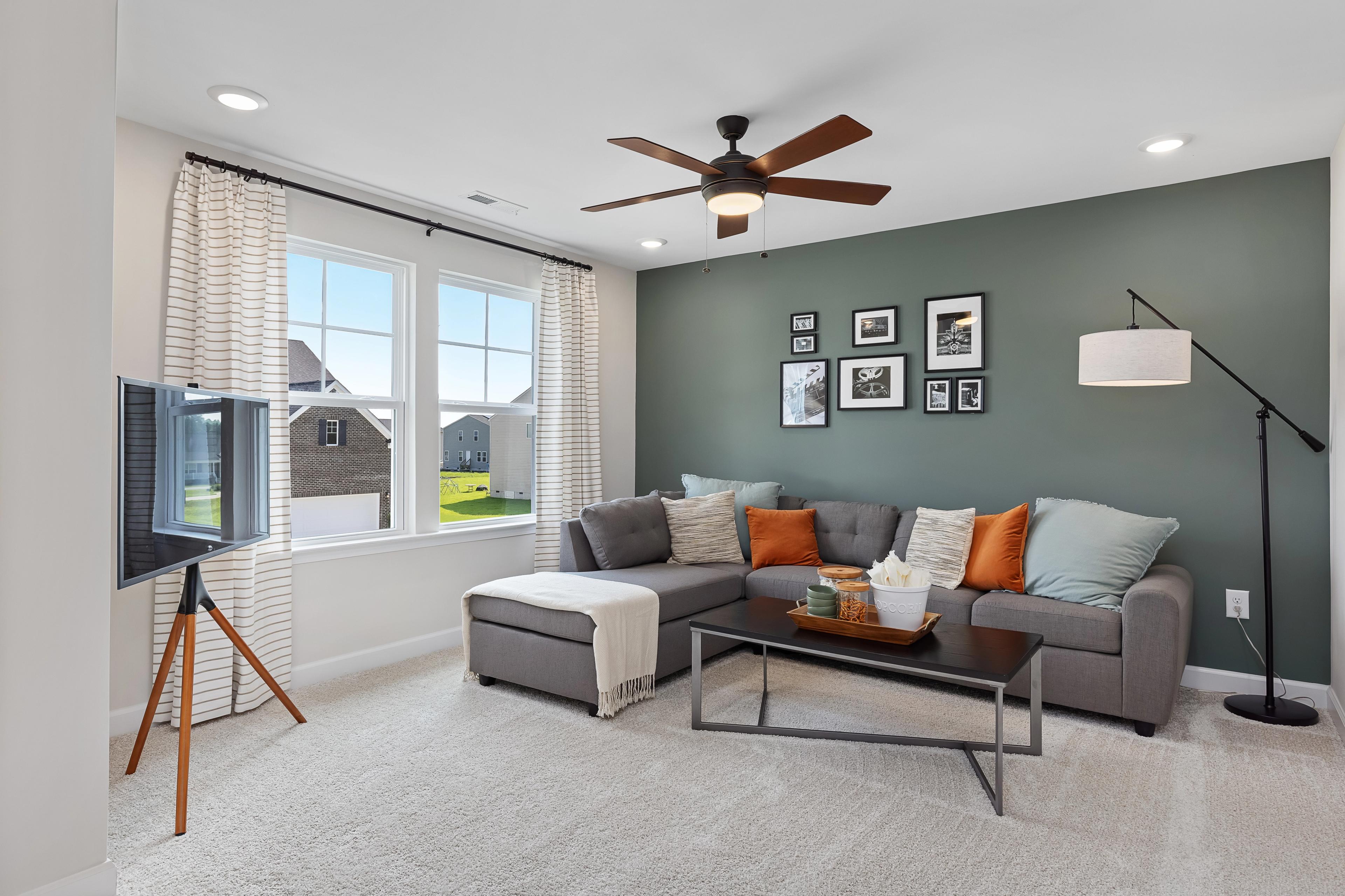 Cozy living room with gray L-shaped sofa, orange pillows, wall art, and large windows at Woodland Crossing in Zebulon, NC