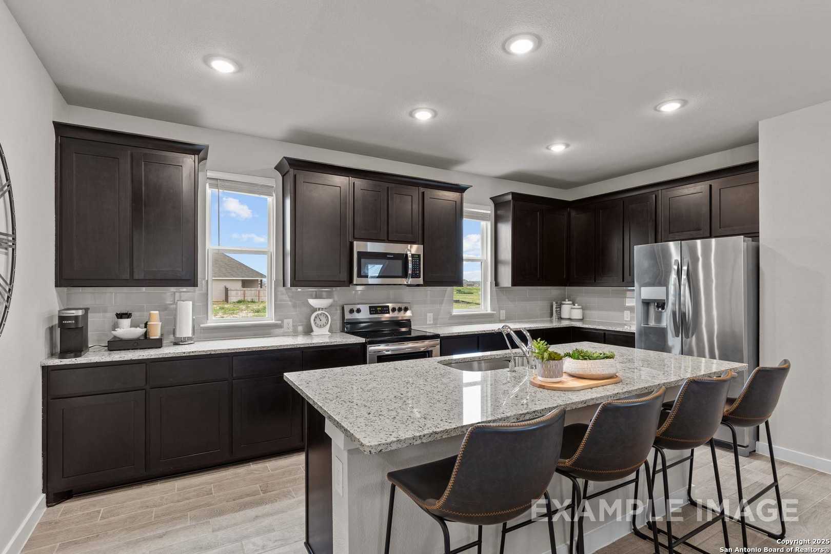 Modern kitchen with dark cabinets, quartz island, stainless fridge and oven in The Collin B 3-bedroom home, Seguin, Texas