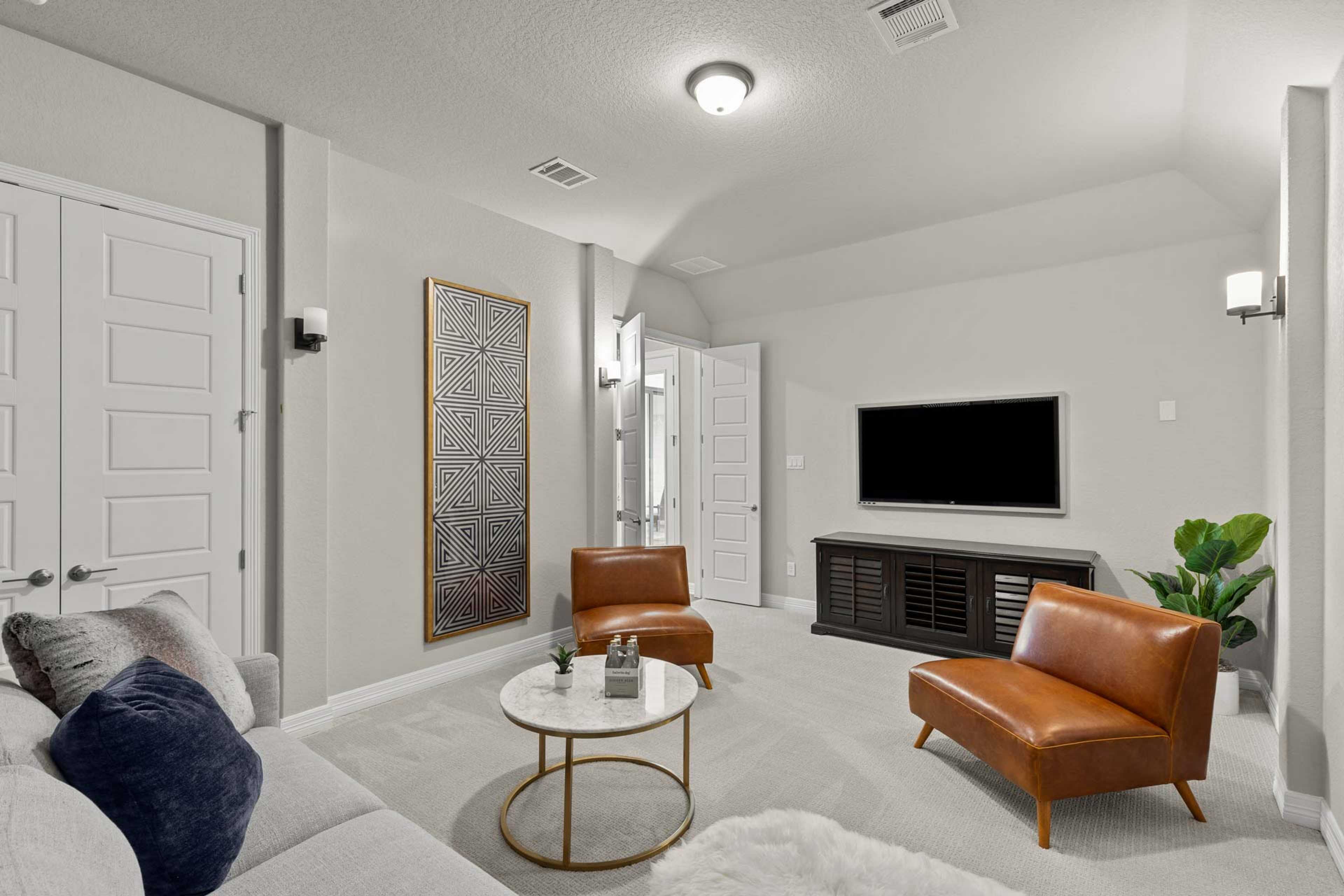 Cozy media room at Potranco Oaks in Castroville Texas by Davidson Homes with gray sofa, leather chairs, wall TV, and abstract art