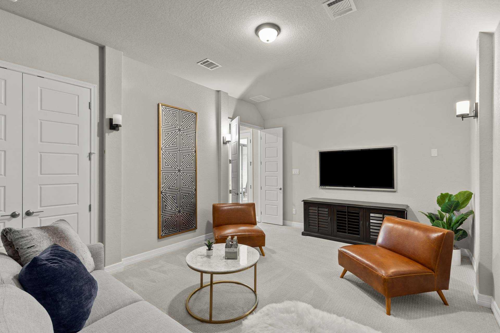 Cozy media room in The Summerlin B home design with gray sectional sofa, leather armchairs, round coffee table, wall TV, and double doors