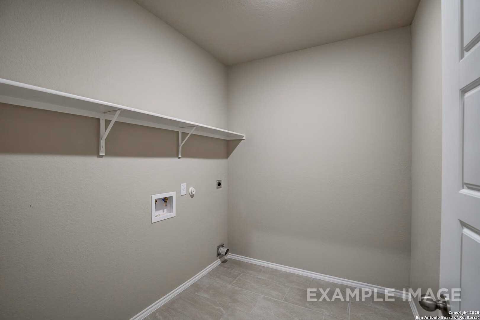 Spacious laundry room with beige walls, white floating shelves, and washer-dryer hookups in Davidson Homes The Murray K, San Antonio