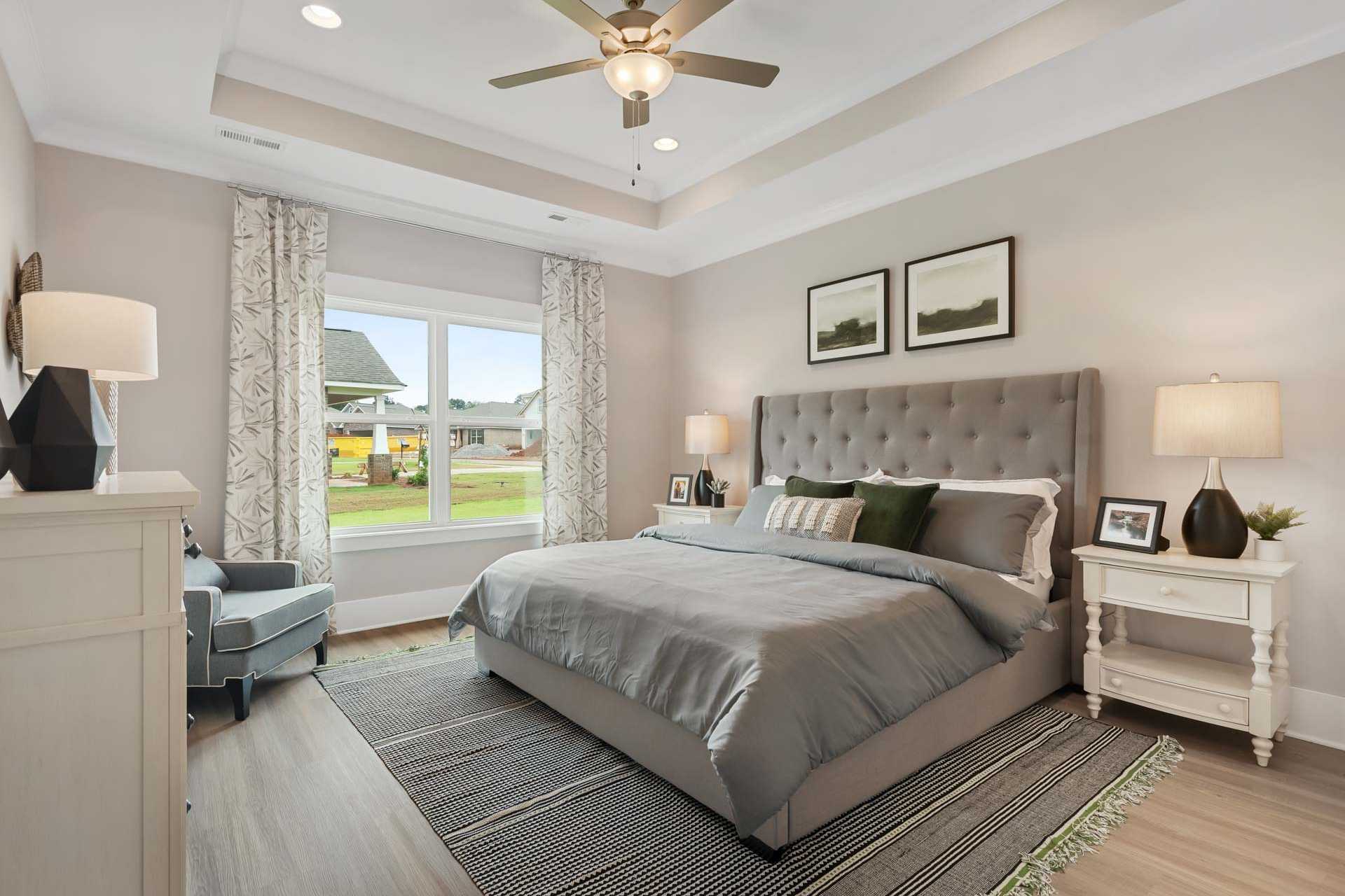 Spacious master bedroom at Durham Farms in Harvest Alabama with gray upholstered bed, hardwood floors, and large windows