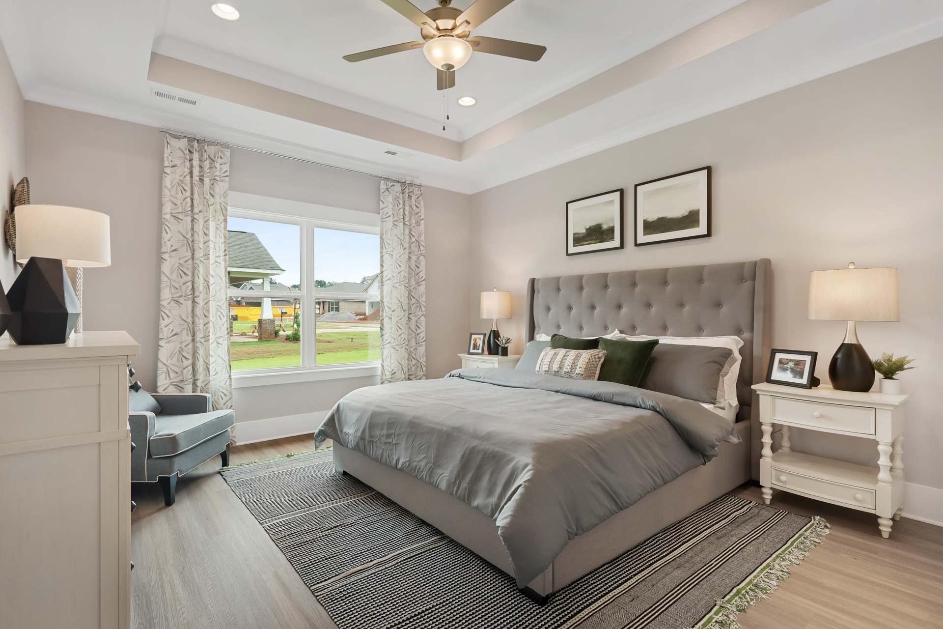 Spacious master bedroom at Durham Farms in Harvest Alabama with gray upholstered bed, hardwood floors, and large windows
