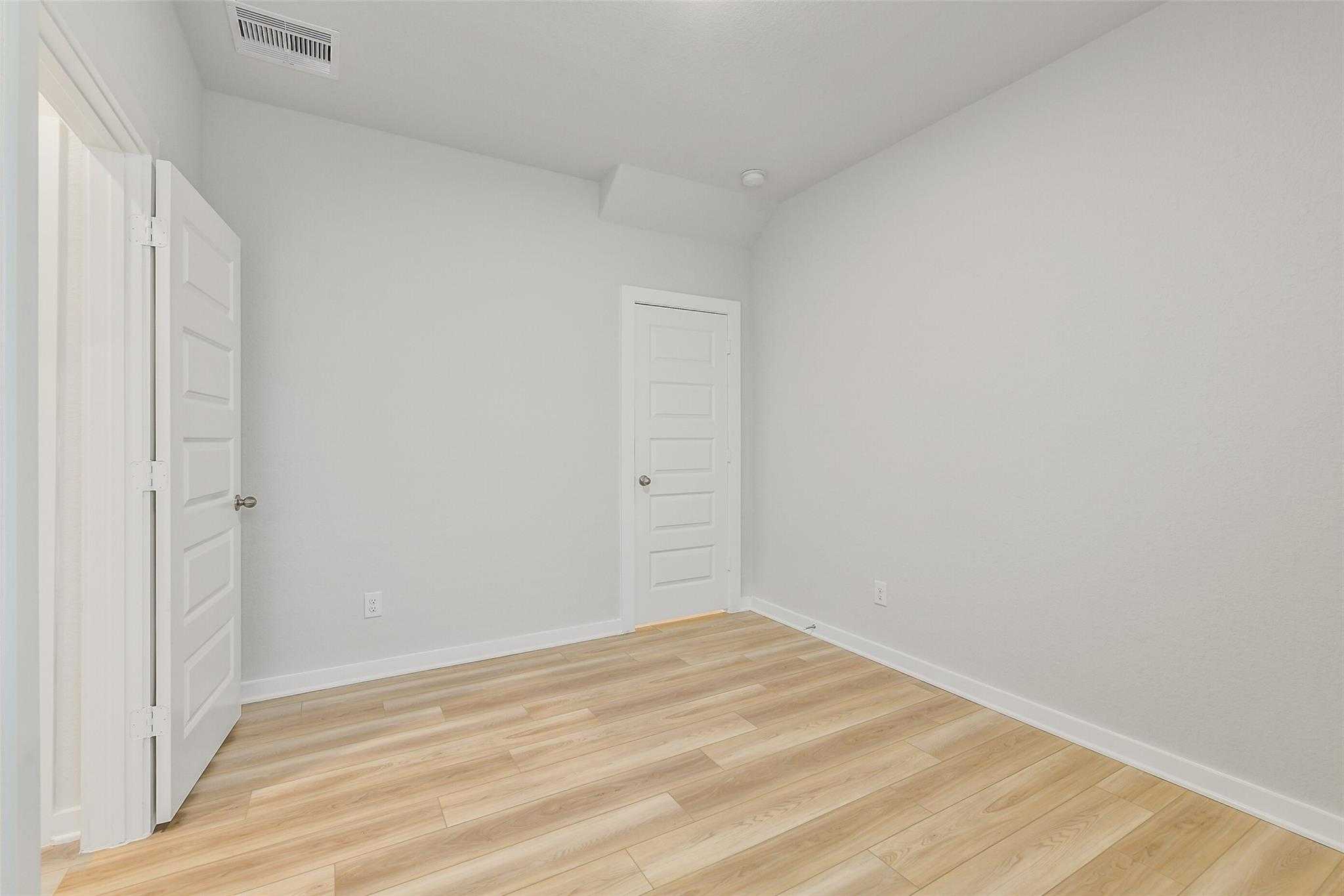 Empty secondary bedroom with light gray walls, wood laminate floors, and double doors in Davidson Homes The Rio Grande H, Magnolia TX