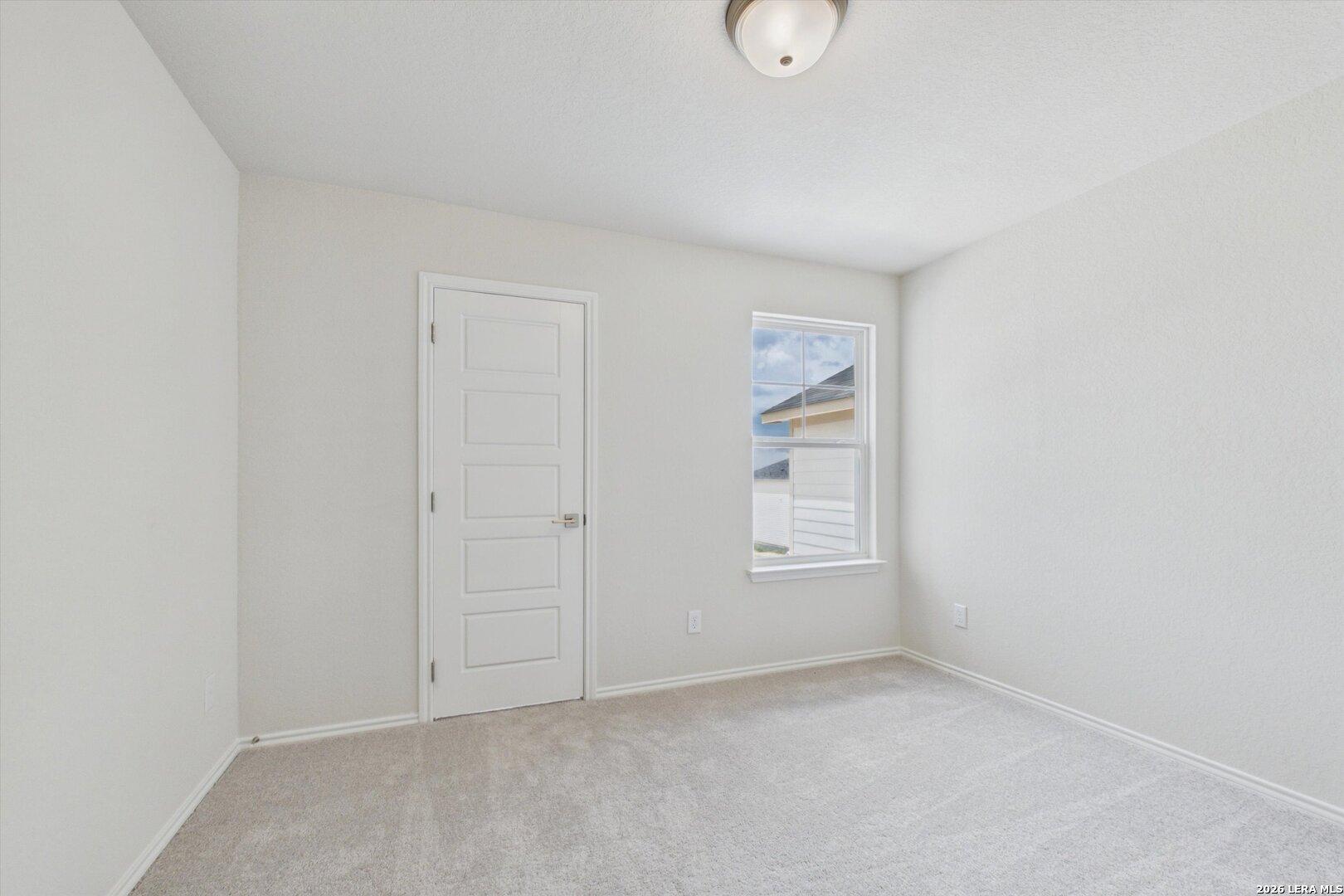 Bright, carpeted bedroom with neutral walls in The Charlotte B floor plan at Meadows at Oak Creek, San Antonio, Texas.
