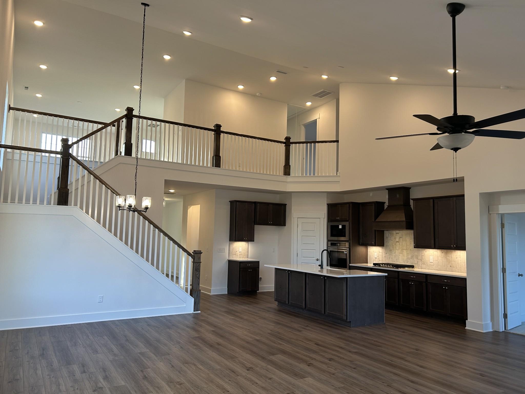 Two-story foyer with wooden staircase, open kitchen featuring dark cabinets, island, and recessed lighting in The Ridgeport F, Mt. Juliet, TN