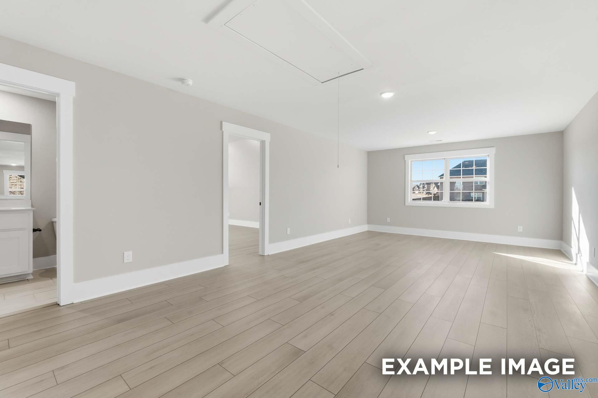 Spacious master bedroom with hardwood floors, large window, and adjacent en-suite bathroom in Davidson Homes The Emory, Decatur AL