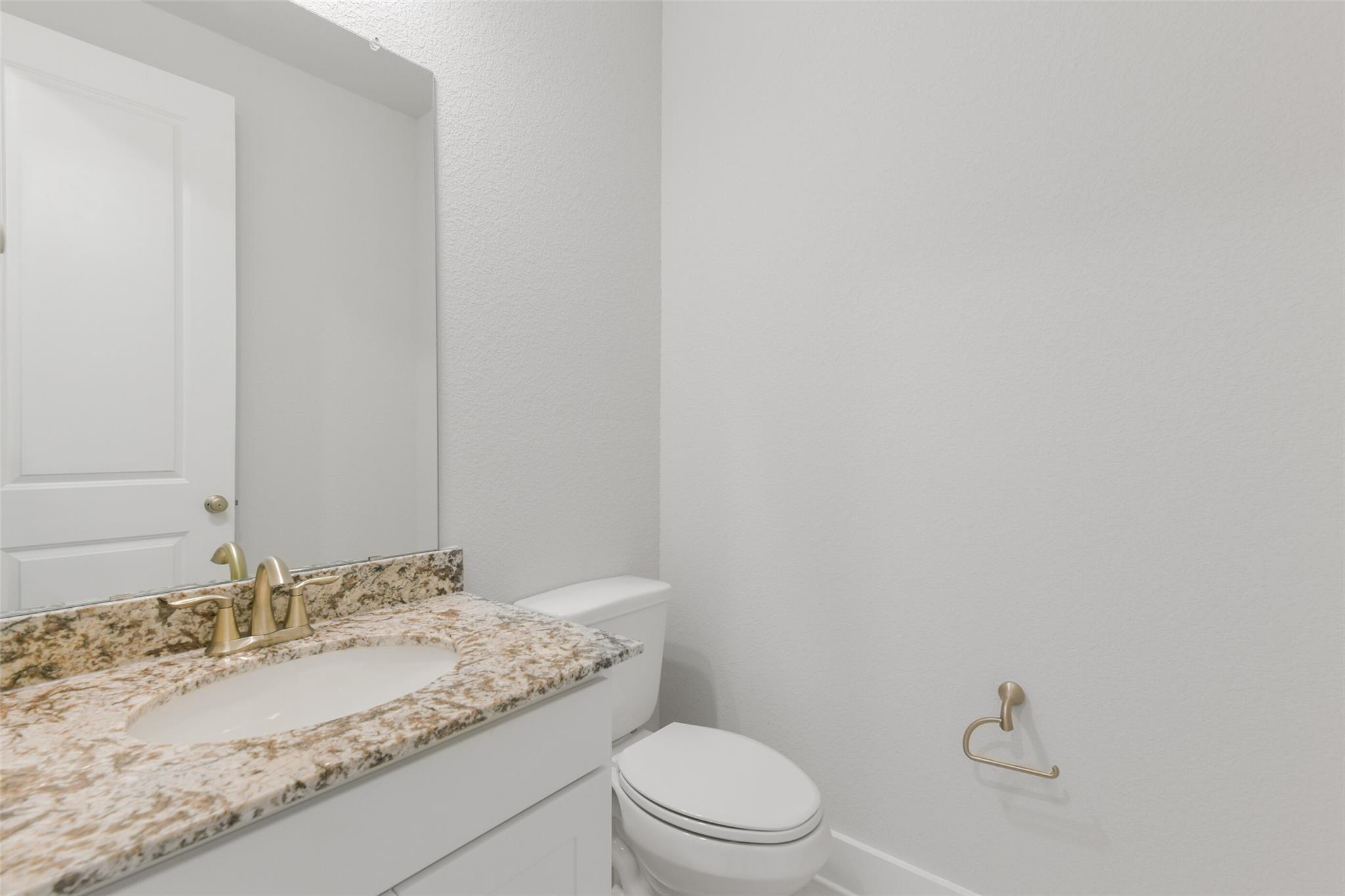 Elegant powder room with granite vanity, vessel sink, gold faucet, and white toilet in Davidson Homes The Edward A, Lago Mar, Texas City