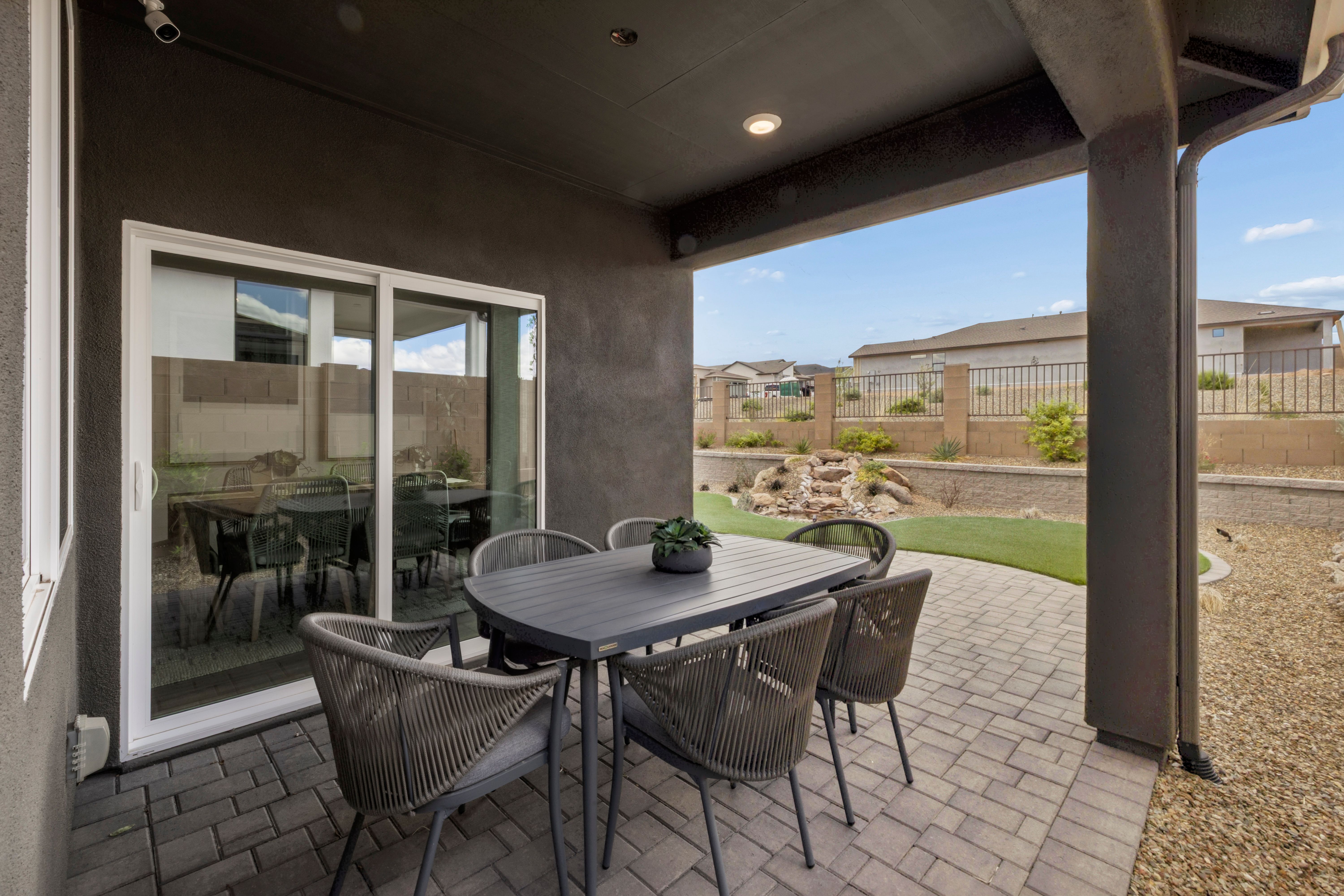 Covered patio with wicker dining set at South Ranch in Prescott AZ featuring rock waterfall, turf and desert landscape