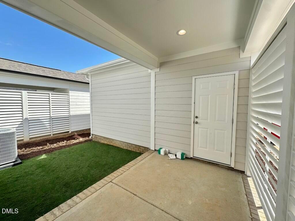 Covered back patio with white door, shutters, AC unit, and lush green lawn in Davidson Homes The Burke, Knightdale, NC