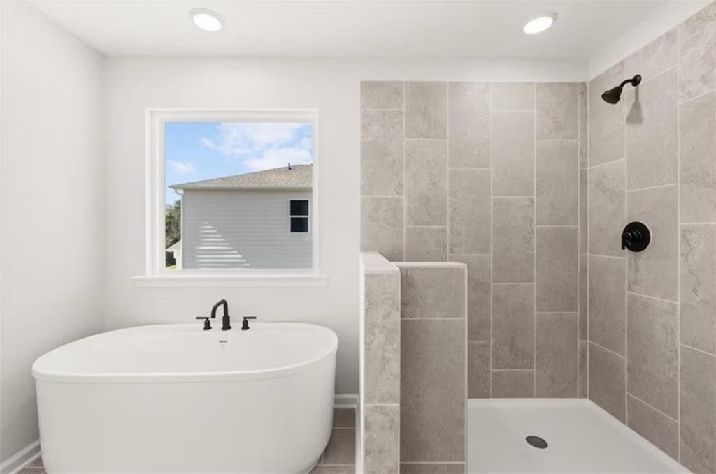 Luxurious master bathroom with freestanding soaking tub and gray tiled walk-in shower in Davidson Homes The Hickory B, Winder GA