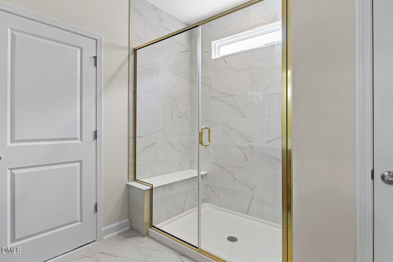 Elegant marble-tiled walk-in shower with gold frame and built-in bench in The Birch II C home, Sage on North Main, Wake Forest, NC