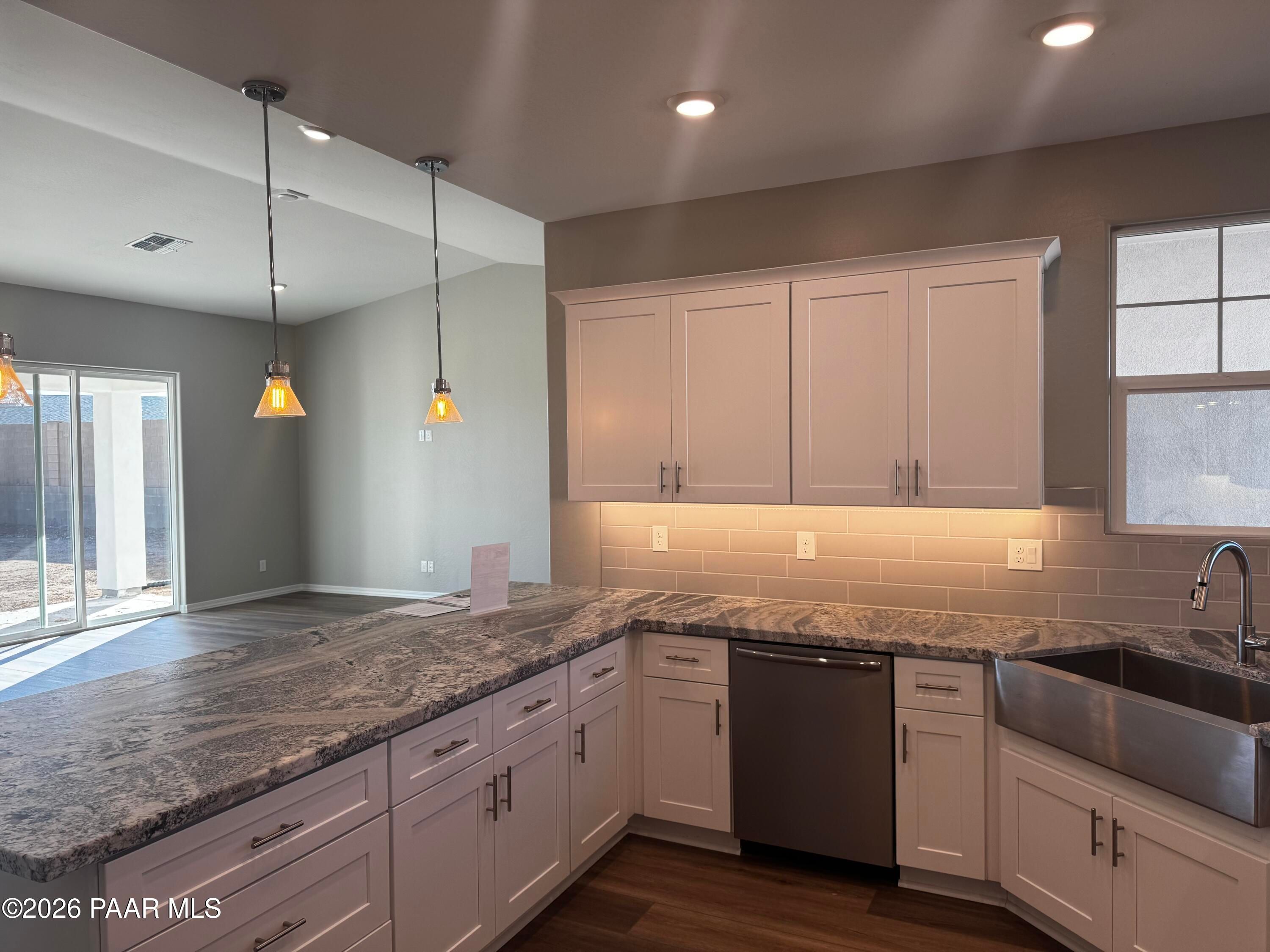Modern white kitchen with veined granite counters, farmhouse sink, and stainless dishwasher in Davidson Homes Daybreak B, Prescott AZ